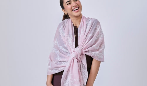 A woman wearing a baby pink cashmere scarf with white lace details around her neck.