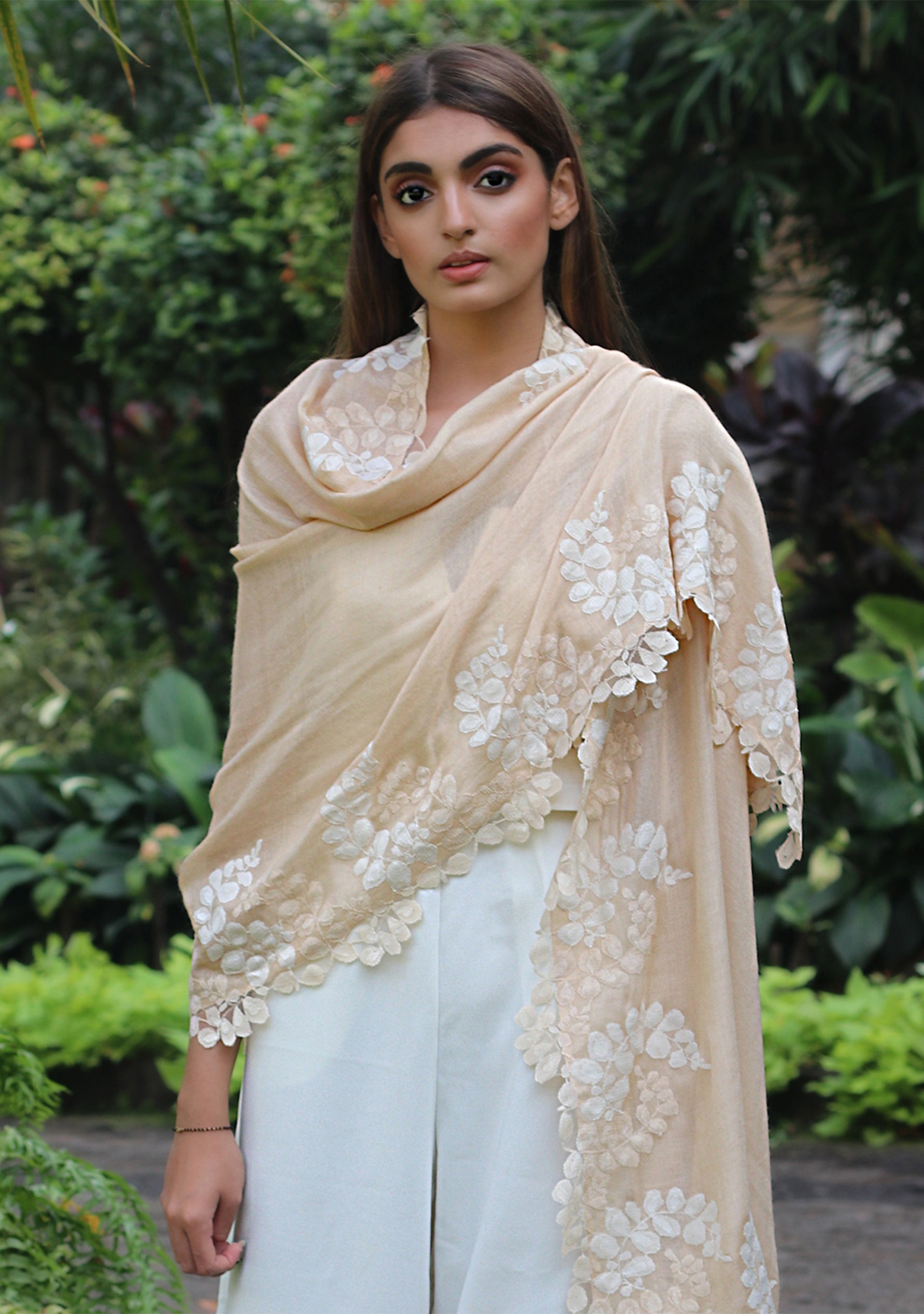 Woman wearing a beige embroidered shawl over a light blue outfit in a garden setting