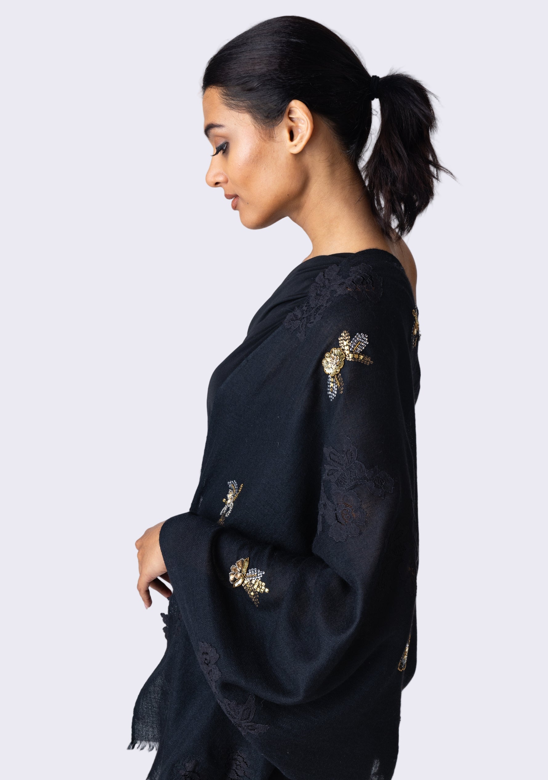 A woman wearing a black cashmere scarf with metallic hand-embroidery and black lace, side profile.