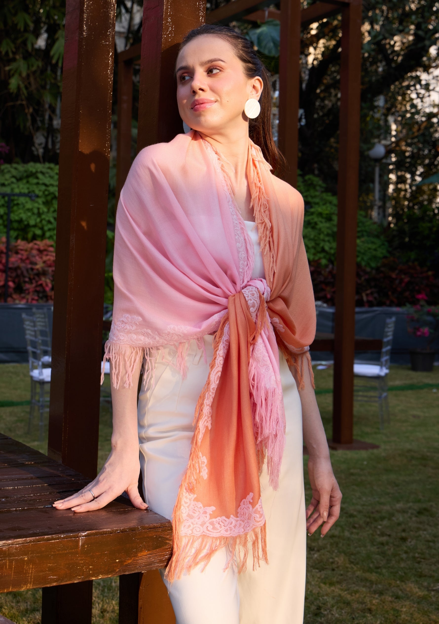 Woman wearing a pink and peach gradient scarf with fringe, standing outdoors.
