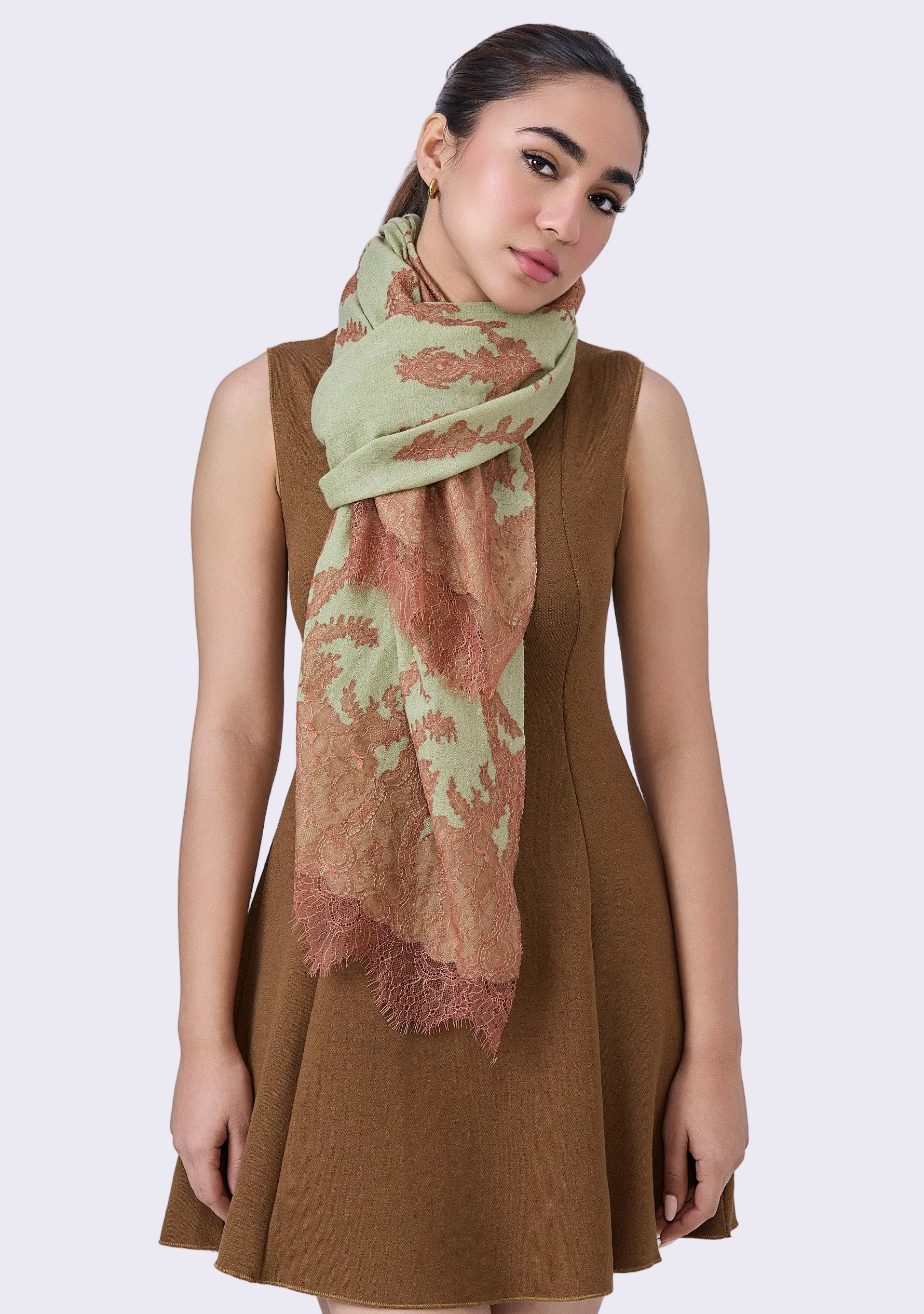 A woman wearing a brown dress and the Fern Green Cashmere Scarf Mocha Mousse Lace around her neck, standing against a neutral background.