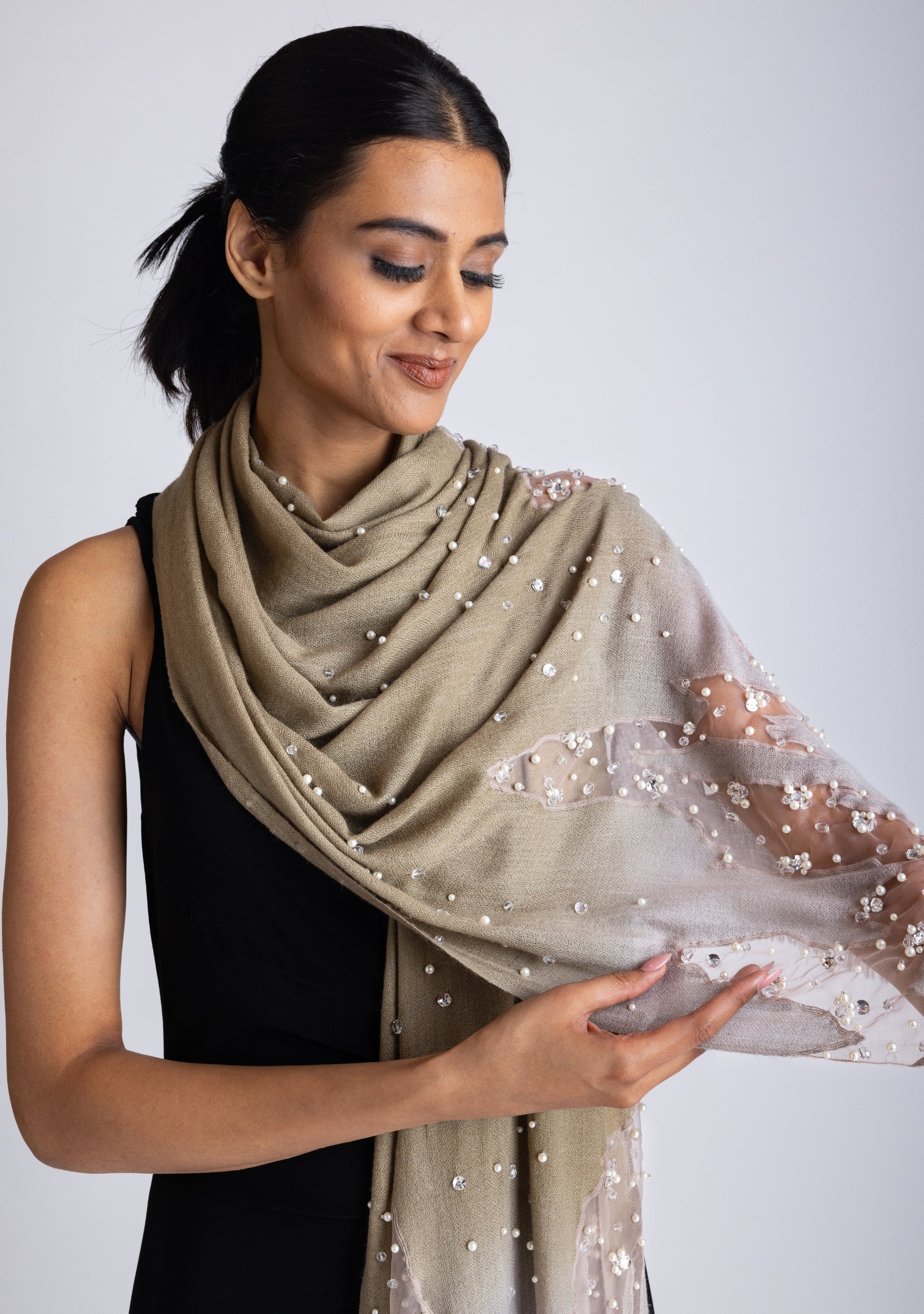 A woman wearing a mousse-khaki cashmere scarf with silver rhinestones and white pearls.