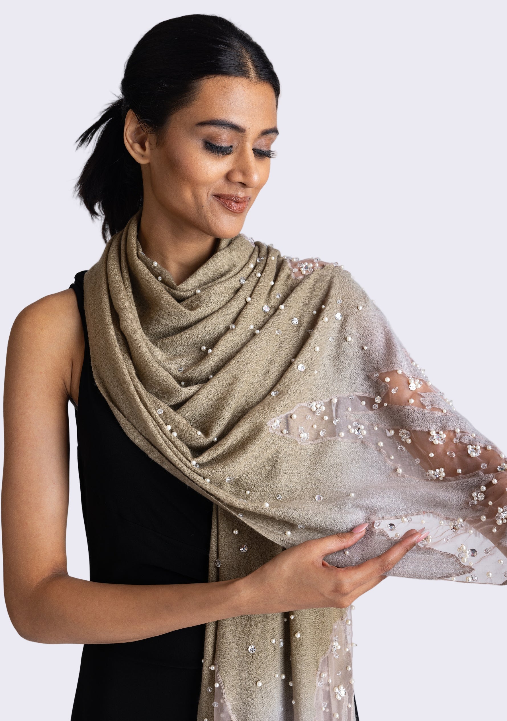 A woman wearing a mousse-khaki cashmere scarf with silver rhinestones and white pearls.