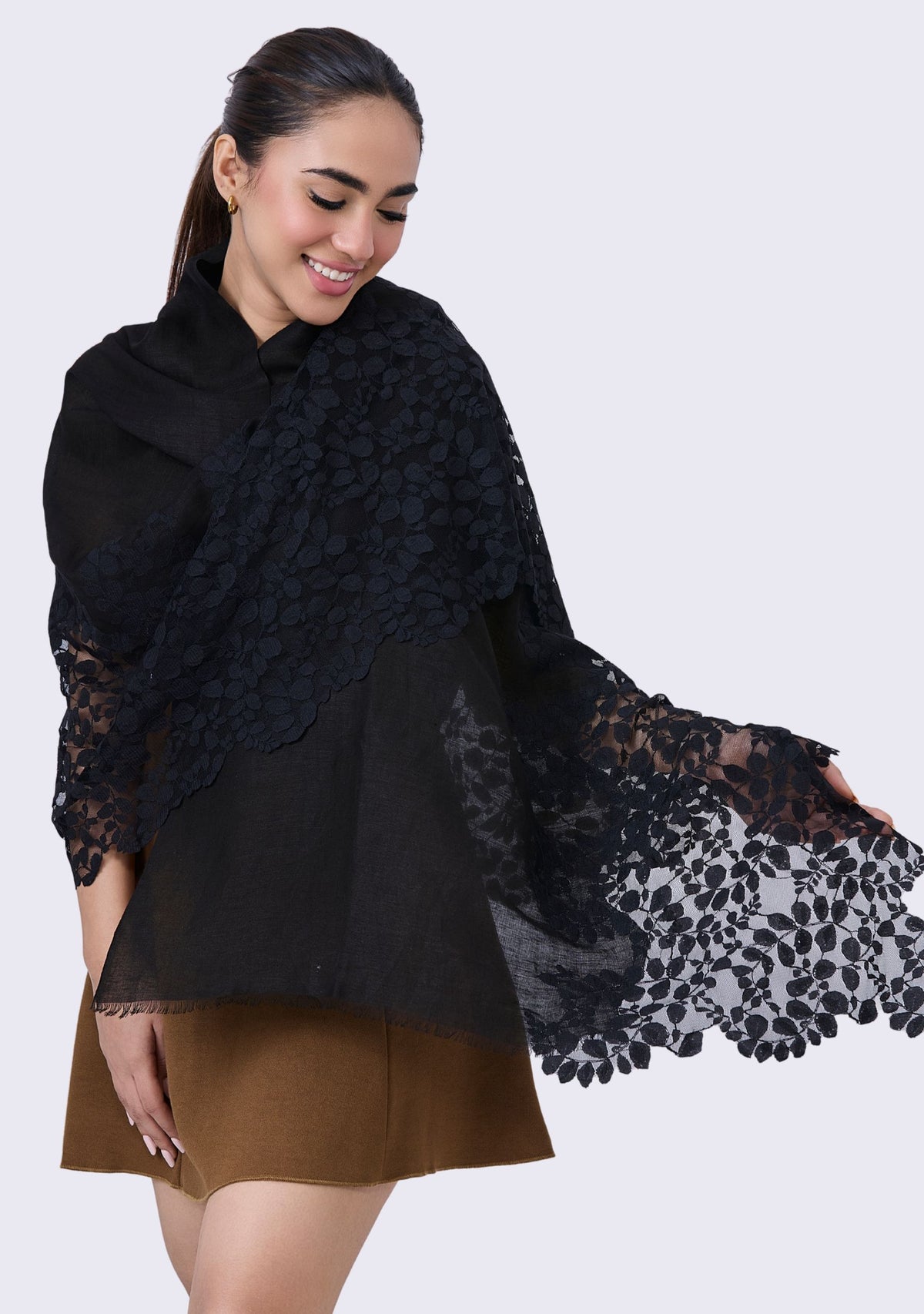 Woman wearing a black lace shawl over a black top and brown skirt on a white background
