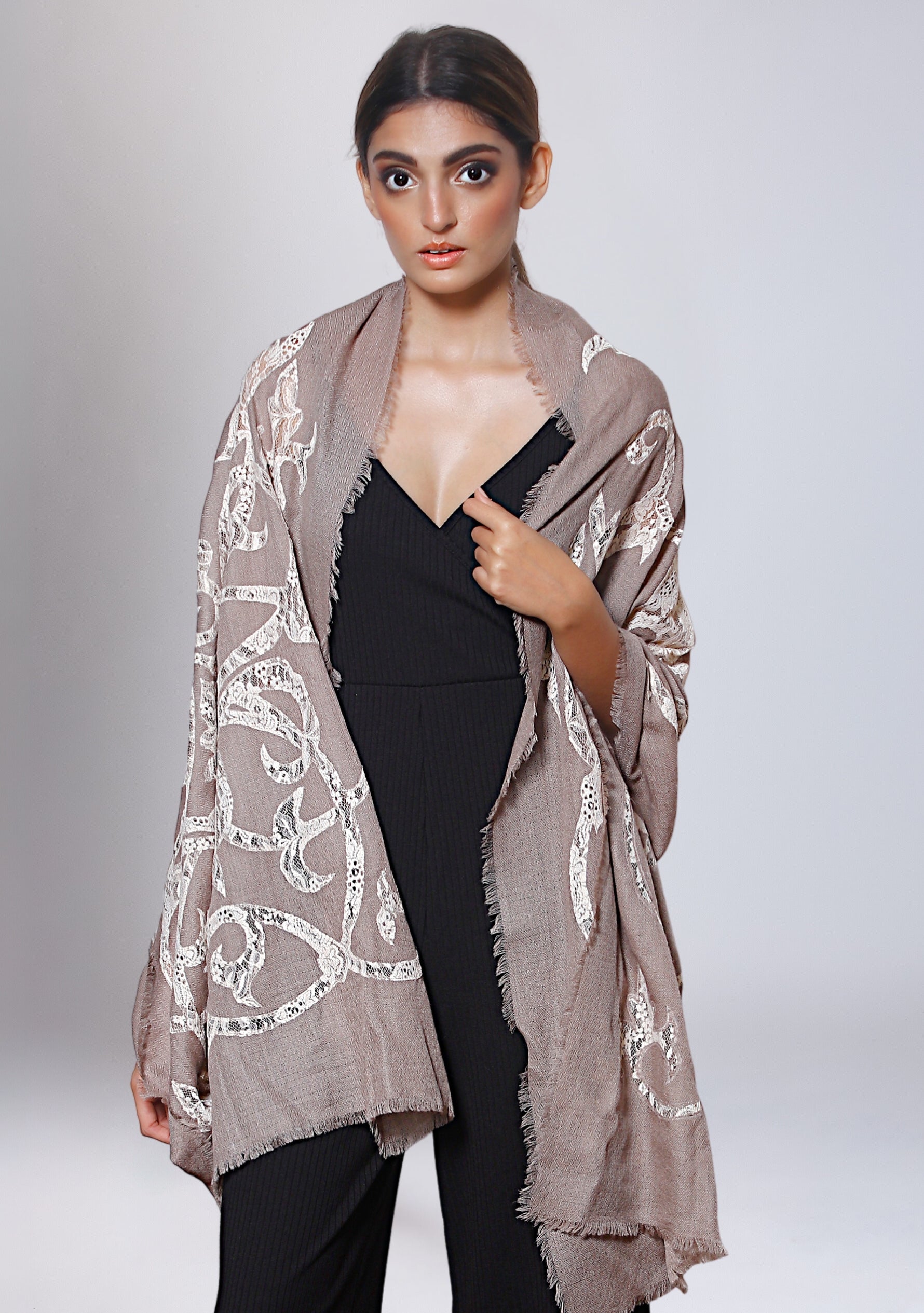 A woman wearing a taupe cashmere scarf with beige lace cutouts, paired with a black top and black pants.