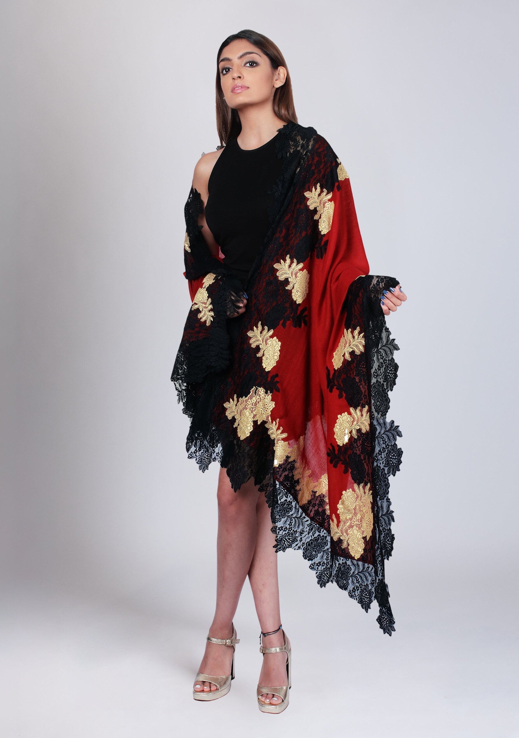 A model wearing a maroon wool and silk scarf with a black and dark gold double color lace border, paired with a black outfit.