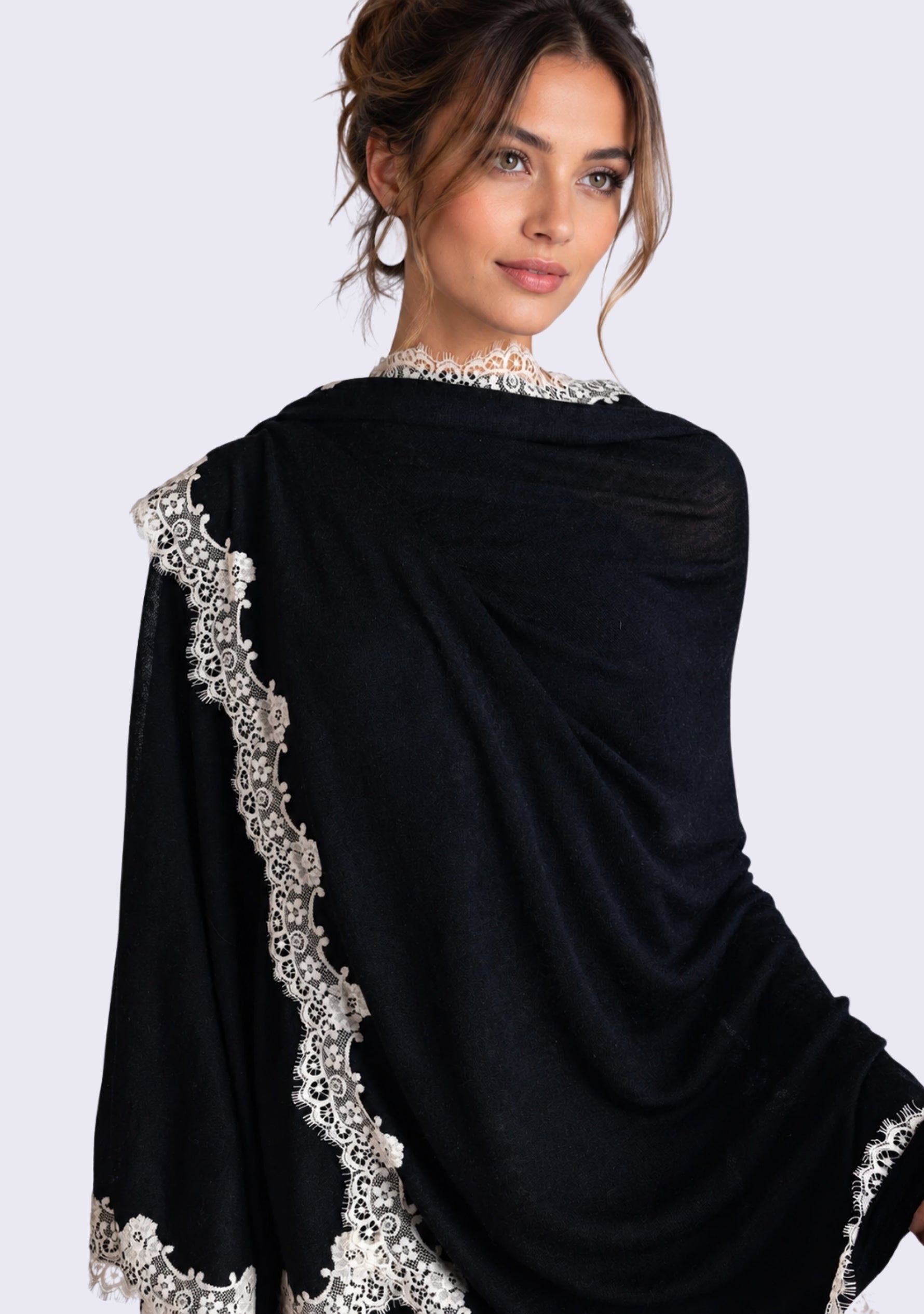 A woman wearing a Black merino wool cape with beige lace photographed against a light gray studio background.