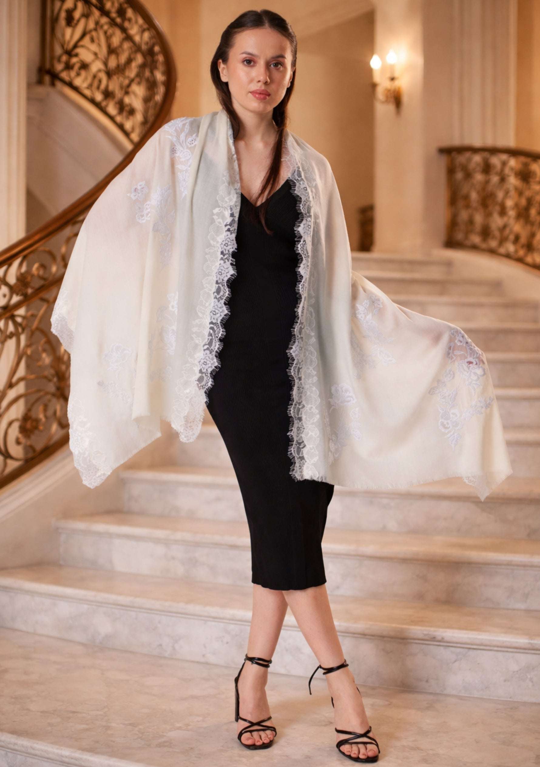 Woman wearing a ivory lace shawl over a black dress in an elegant interior setting.