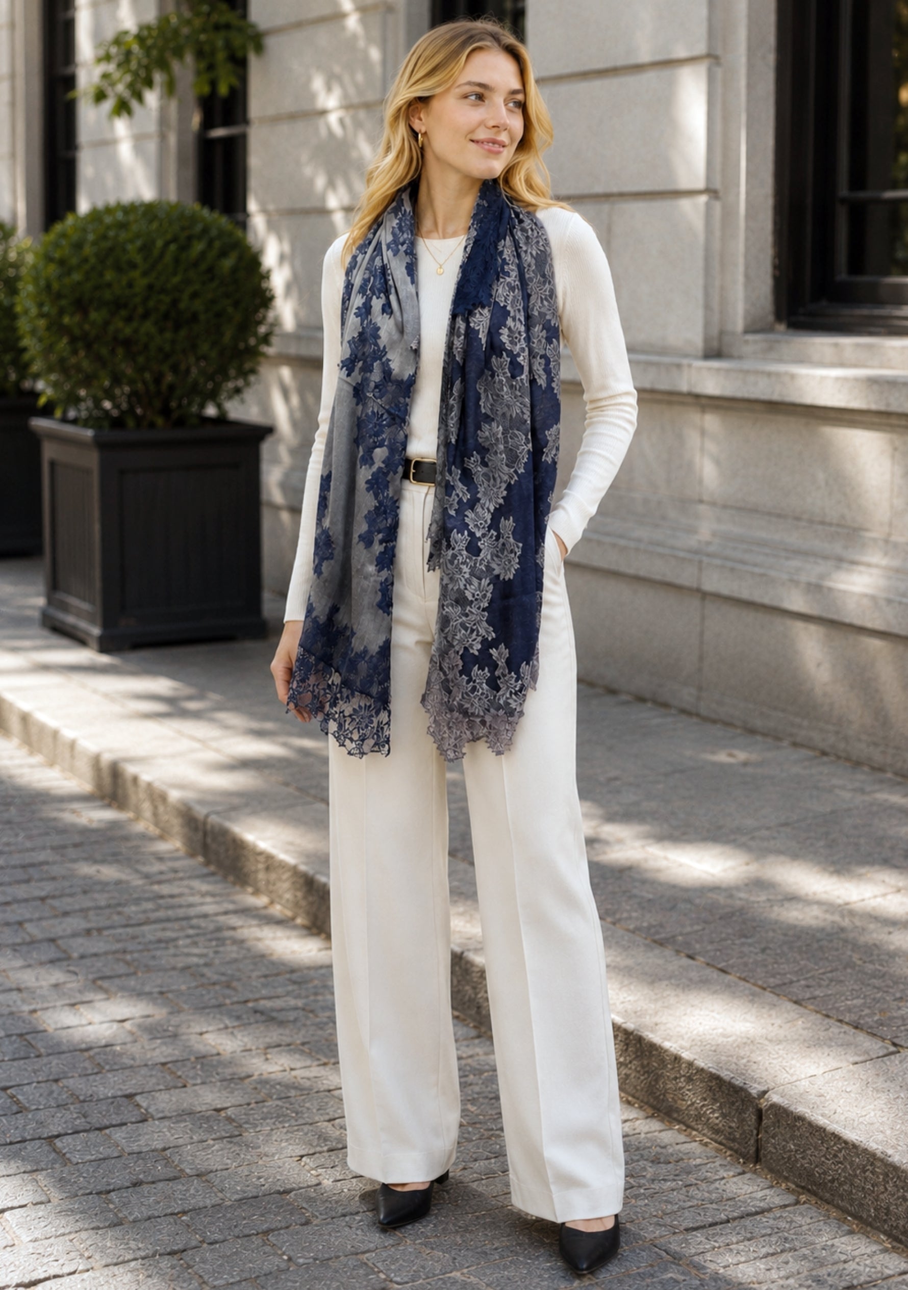 Woman wearing a white outfit with a blue floral scarf on a city street.