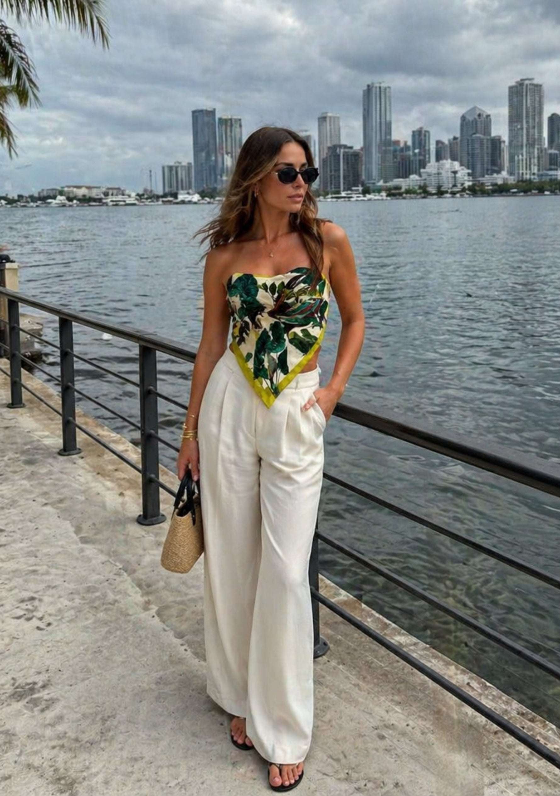 Toucan Print Silk Square Scarf by Maneesha Ruia styled as a chic strapless silk top, featuring a vibrant tropical print with lush green foliage, exotic toucan motifs, and lime green accents, paired with white wide-leg trousers for a luxury resort look.