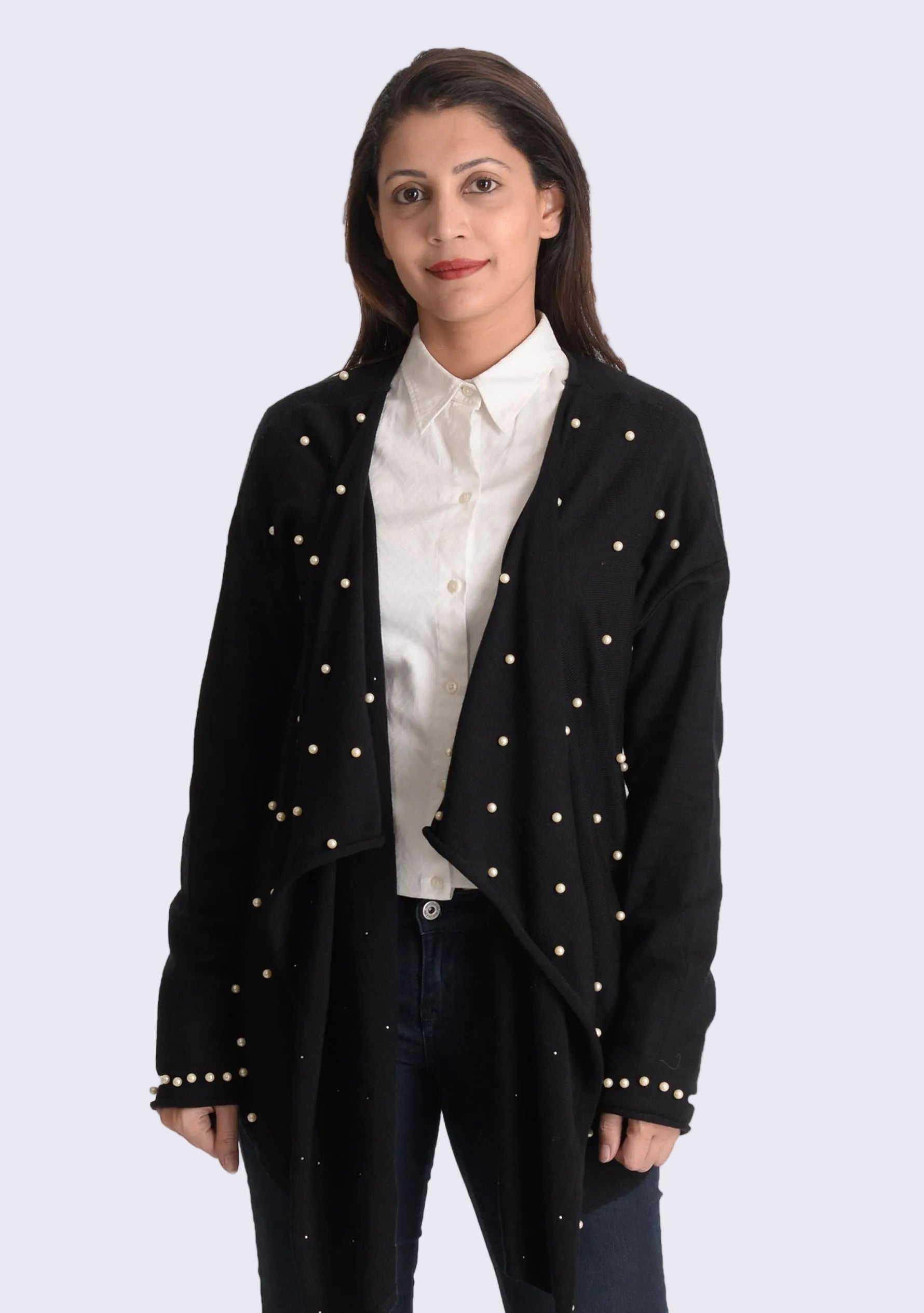 A woman wearing a black long-sleeved wrap cardigan with ivory pearls on the front panels and sleeve cuffs, paired with a white shirt and blue jeans.