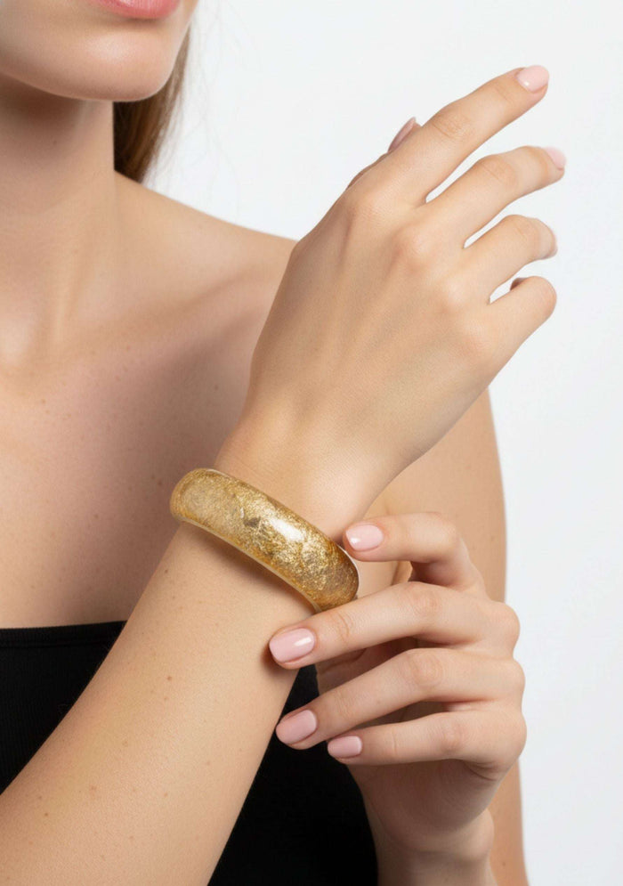 Gold bracelet on a wrist with a plain background