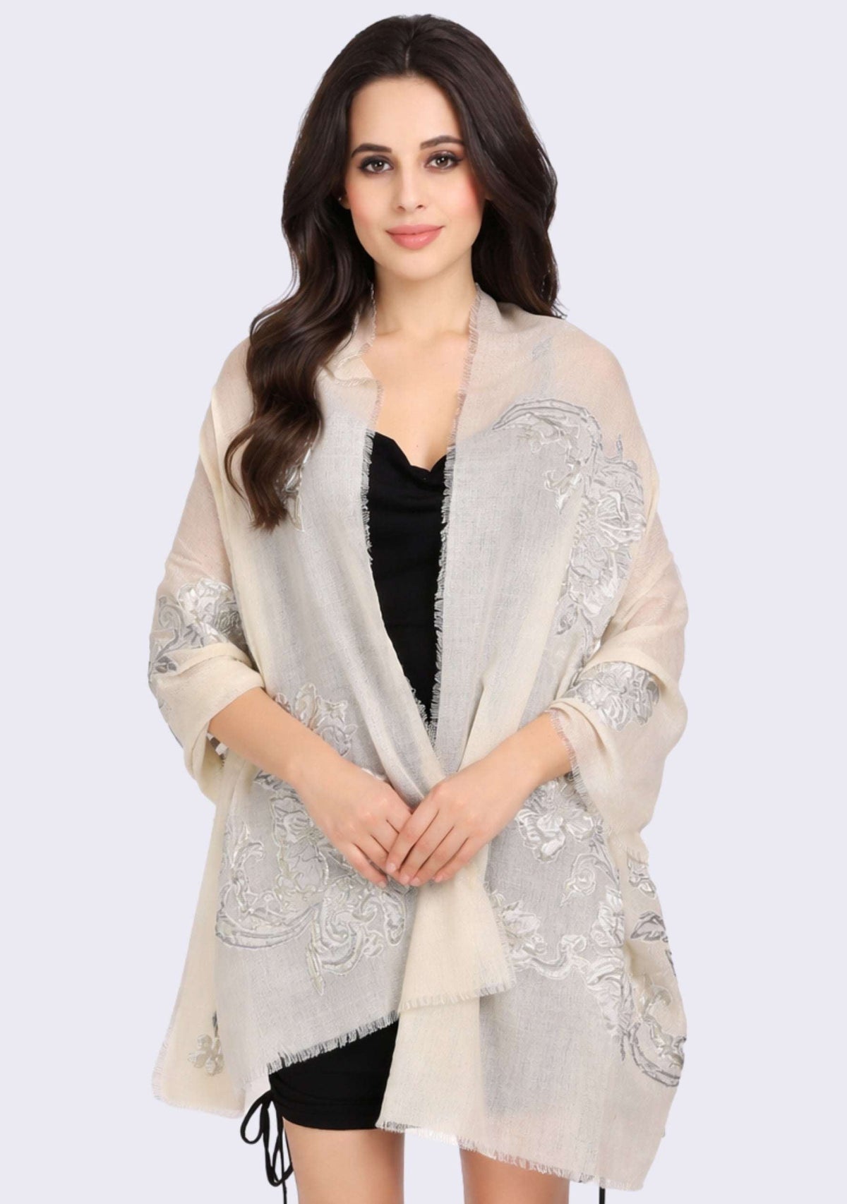 Woman wearing a Maneesha Ruia ivory cashmere embroidered shawl over a black top against a neutral background