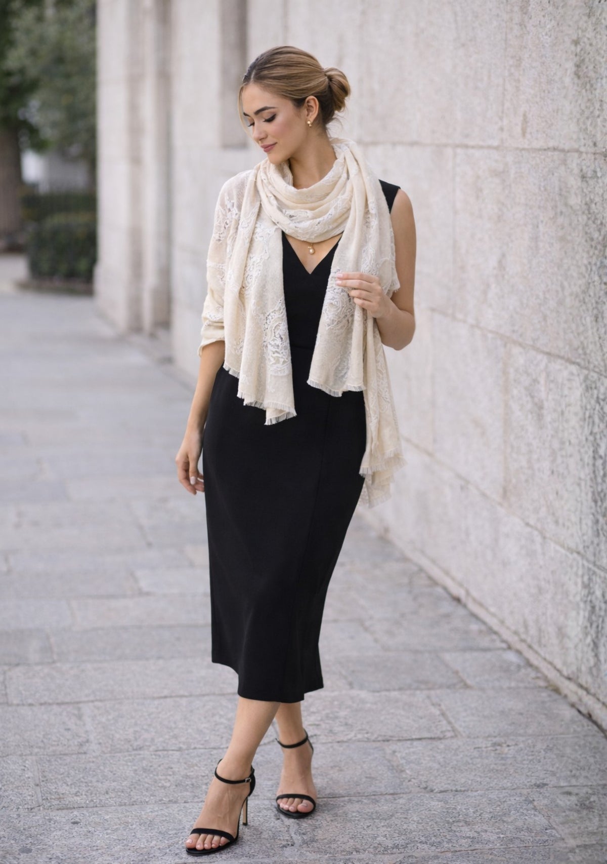 Woman wearing a black dress with a cream scarf against a stone wall.