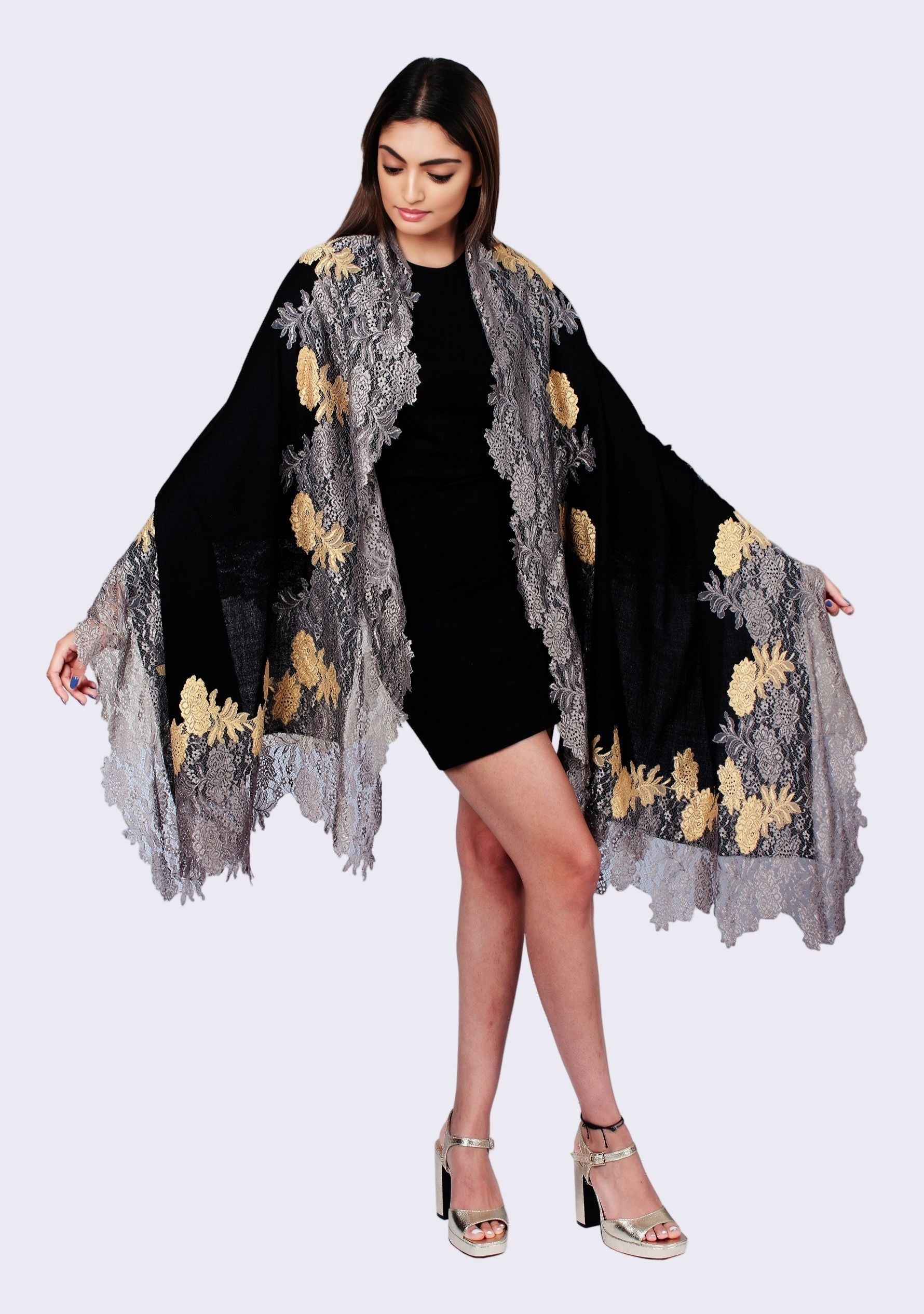 Woman wearing a black dress with a gray lace shawl featuring gold floral patterns on a white background