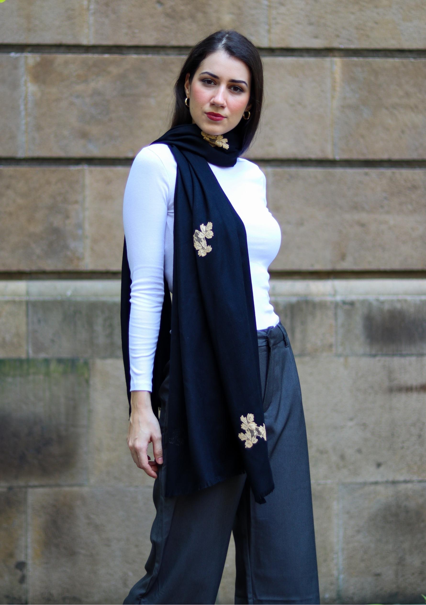 Woman wearing a navy scarf with floral patterns against a stone wall.