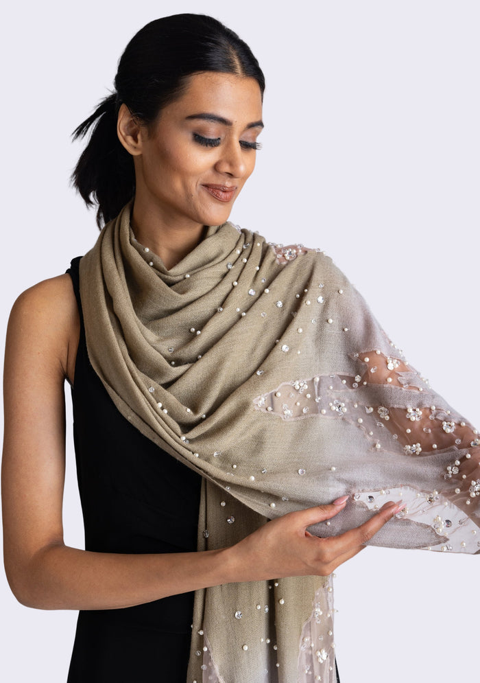 A woman wearing a mousse-khaki cashmere scarf with silver rhinestones and white pearls.
