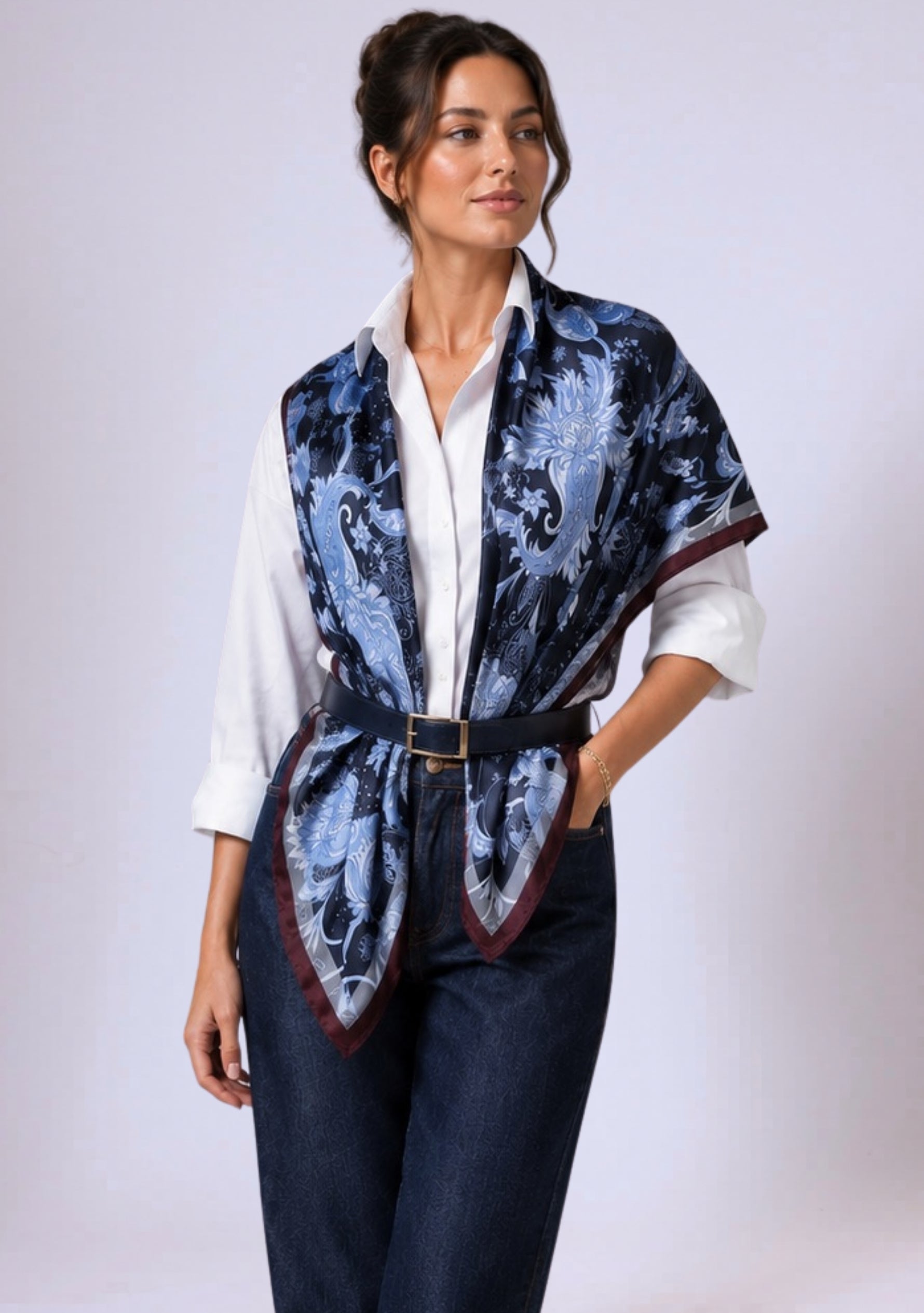 A woman wearing a blue patterned vest silk scarf over a white shirt and dark pants on a white background