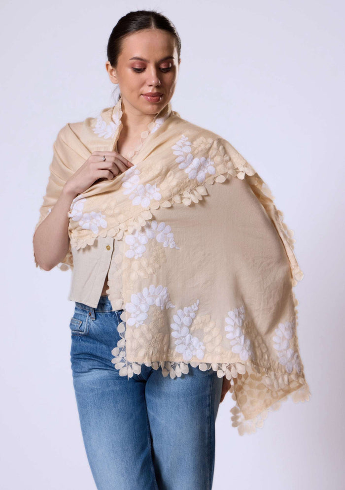 Woman wearing a beige shawl with white floral patterns on a plain background