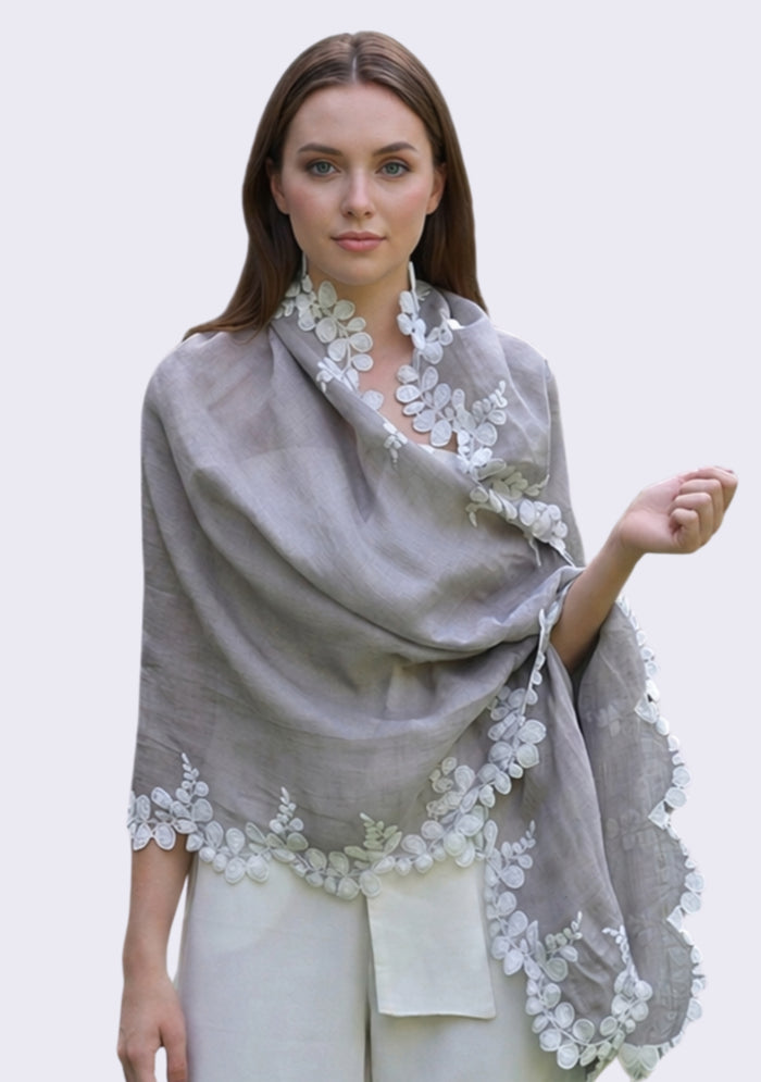 Woman wearing a maneesha ruia gray shawl with floral lace details on a plain background