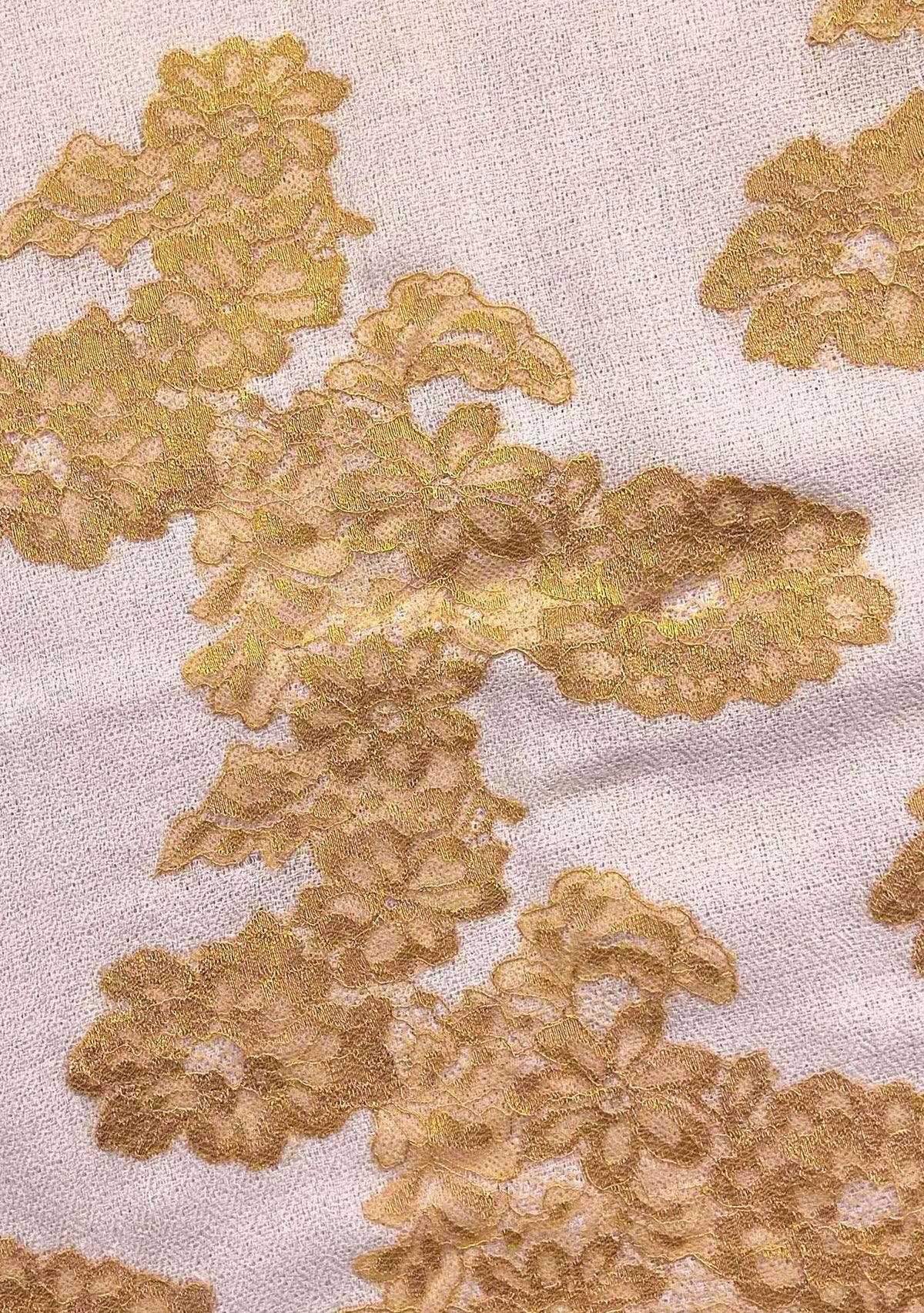 Close-up of handcrafted gold Chantilly lace on a soft beige cashmere scarf, showcasing intricate floral craftsmanship and premium luxury fabric.