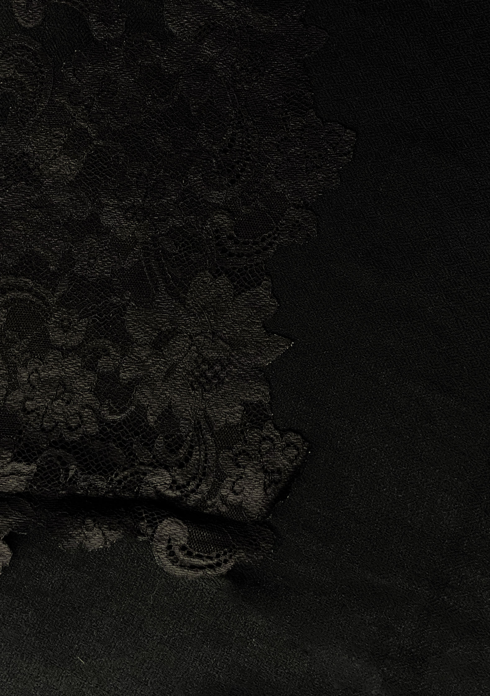 Close-up of black Chantilly floral lace appliqué on a black cashmere scarf, highlighting intricate craftsmanship and premium detailing.