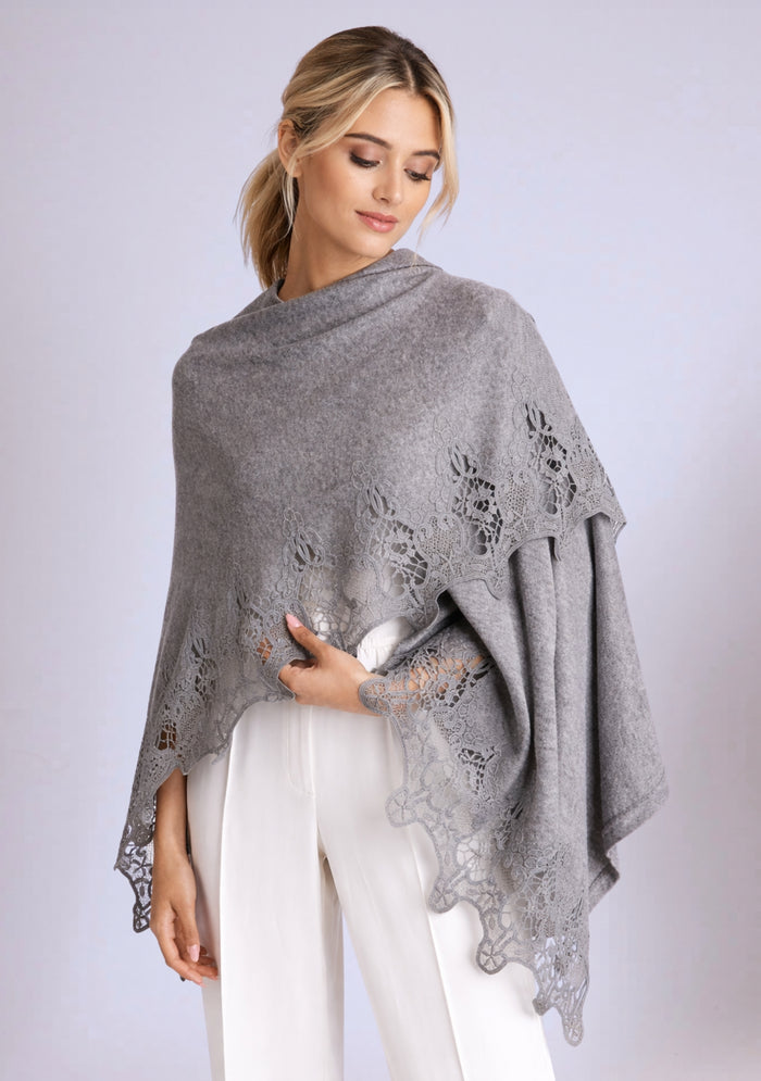 Woman wearing a grey lace and grey fine wool poncho over a white outfit on a light grey background