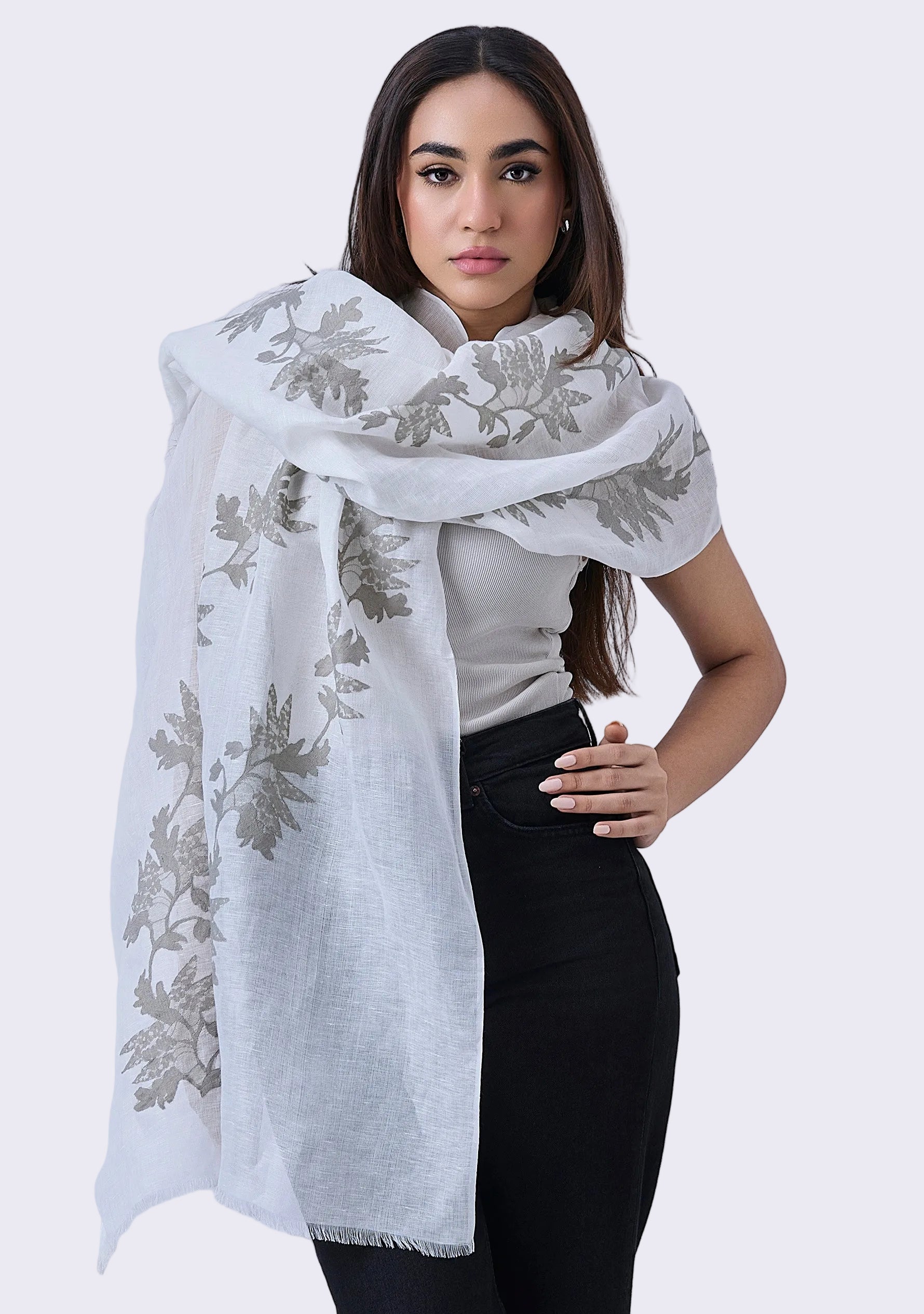 Woman wearing a white scarf with floral embroidery on a plain background
