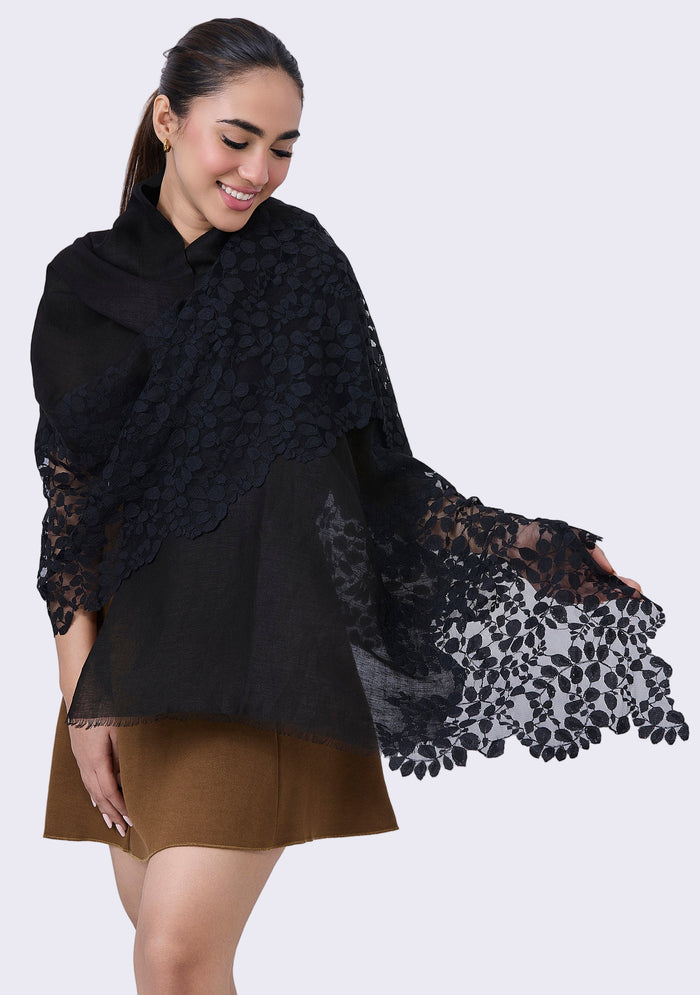 A woman wearing a black linen and modal scarf with a leaf patterned lace, paired with a brown skirt.