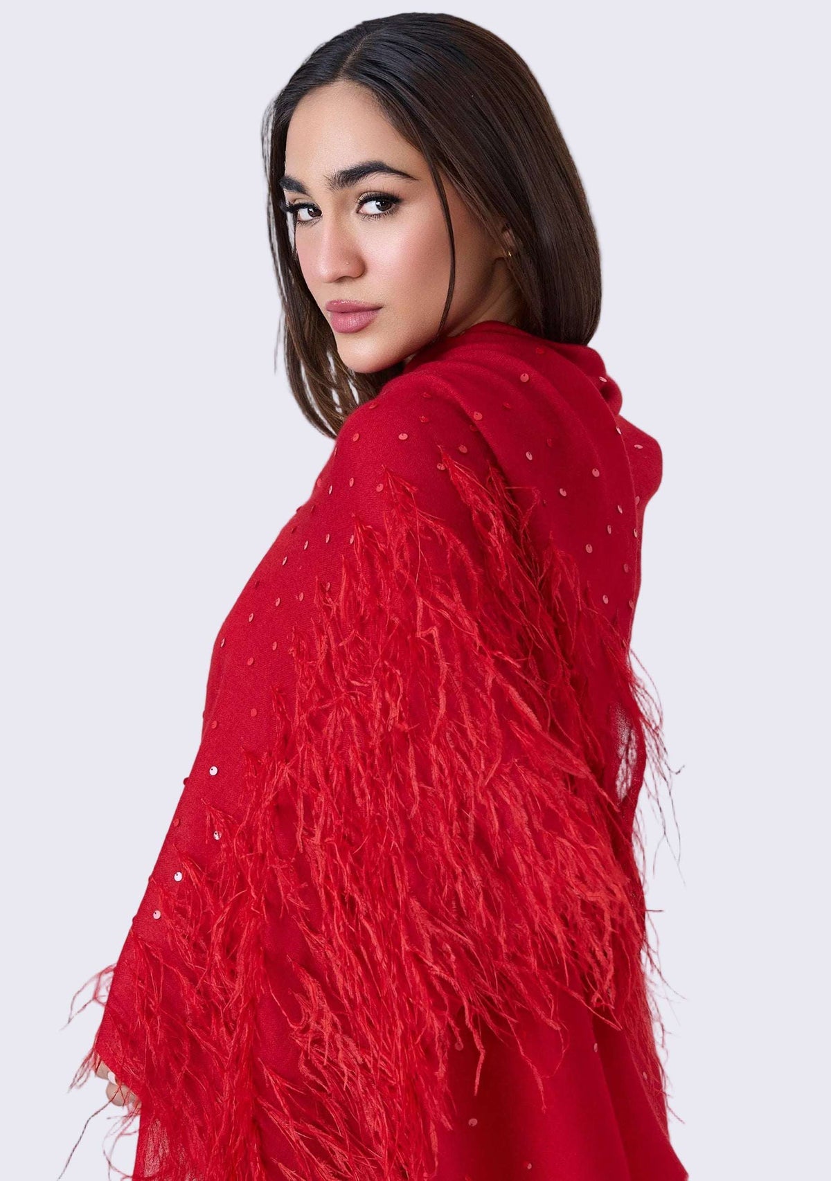 Woman wearing a red feathered shawl against a gray background