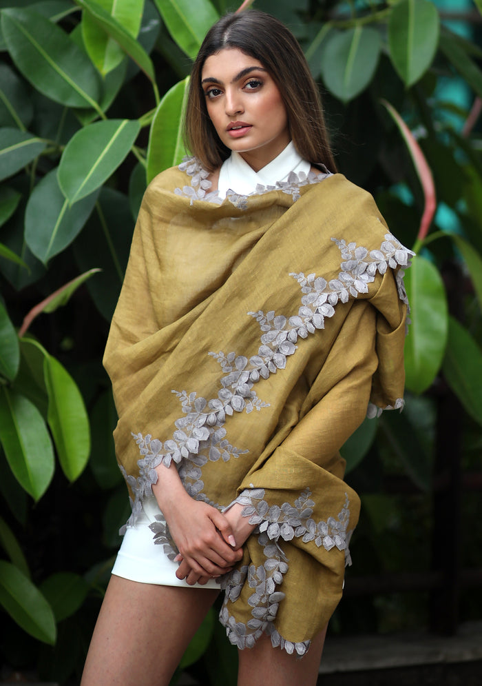 Woman wearing a mustard yellow shawl with floral lace details against a green leafy background