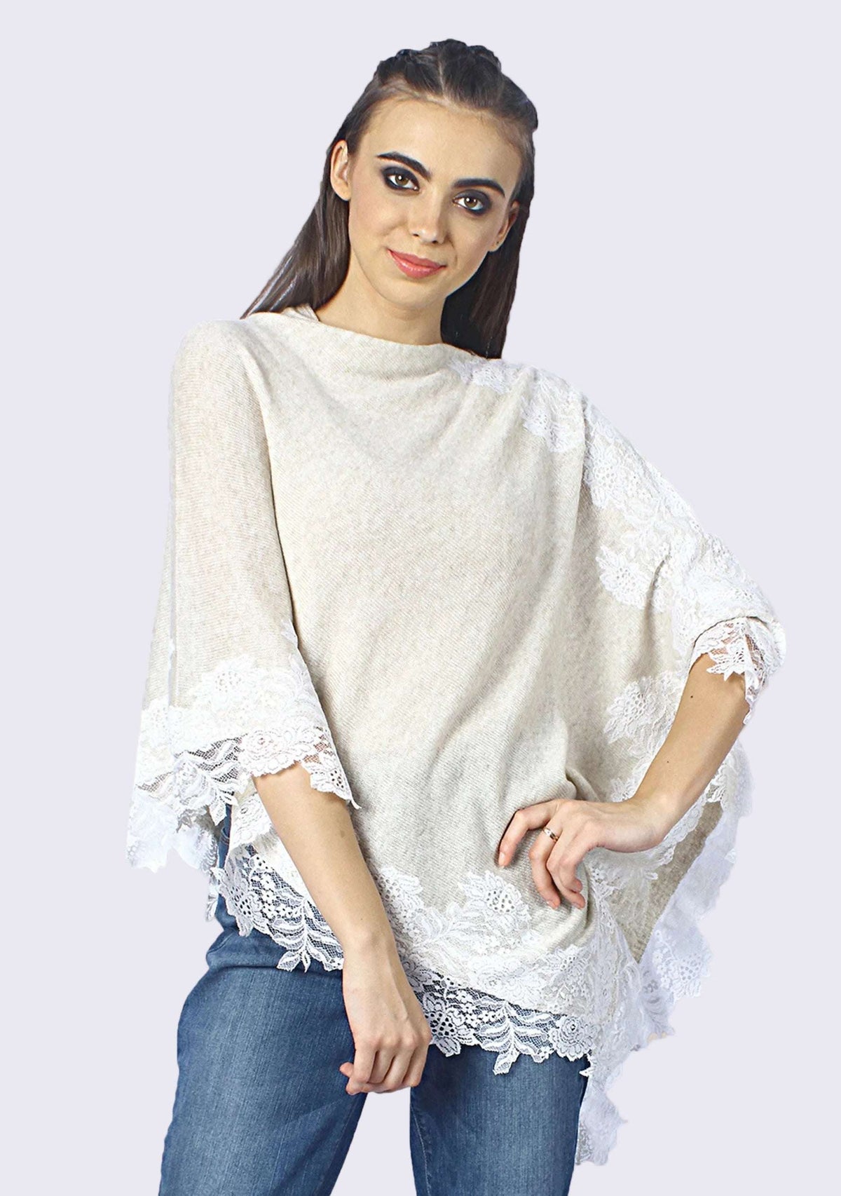 A woman wearing a beige knitted wool poncho with oatmeal floral lace, paired with blue jeans.