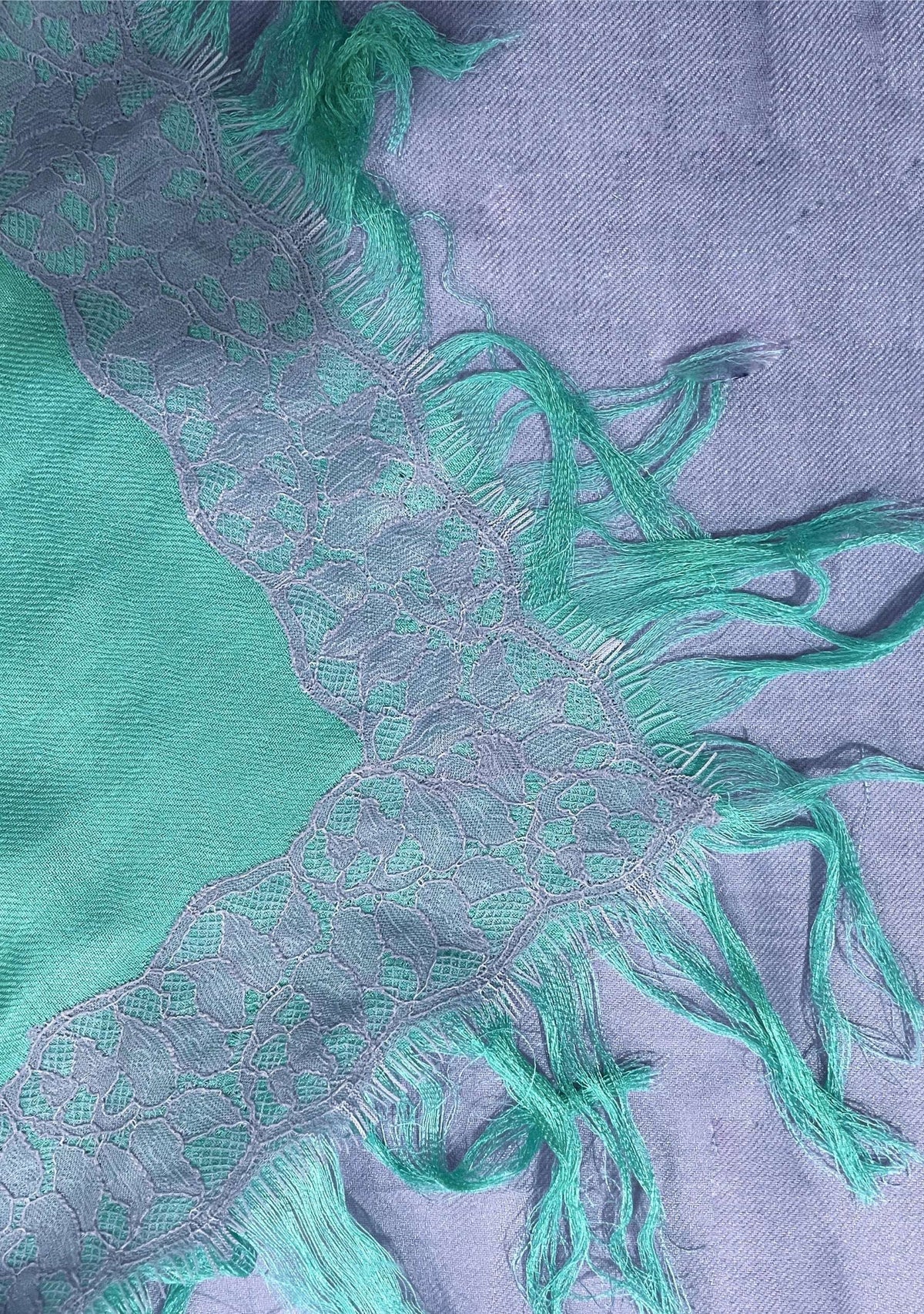 Close-up of the Maneesha Ruia Aqua Ombré Modal & Cashmere Scarf featuring lavender floral lace trim, aqua-to-lavender ombré fabric, and hand-knotted fringes.