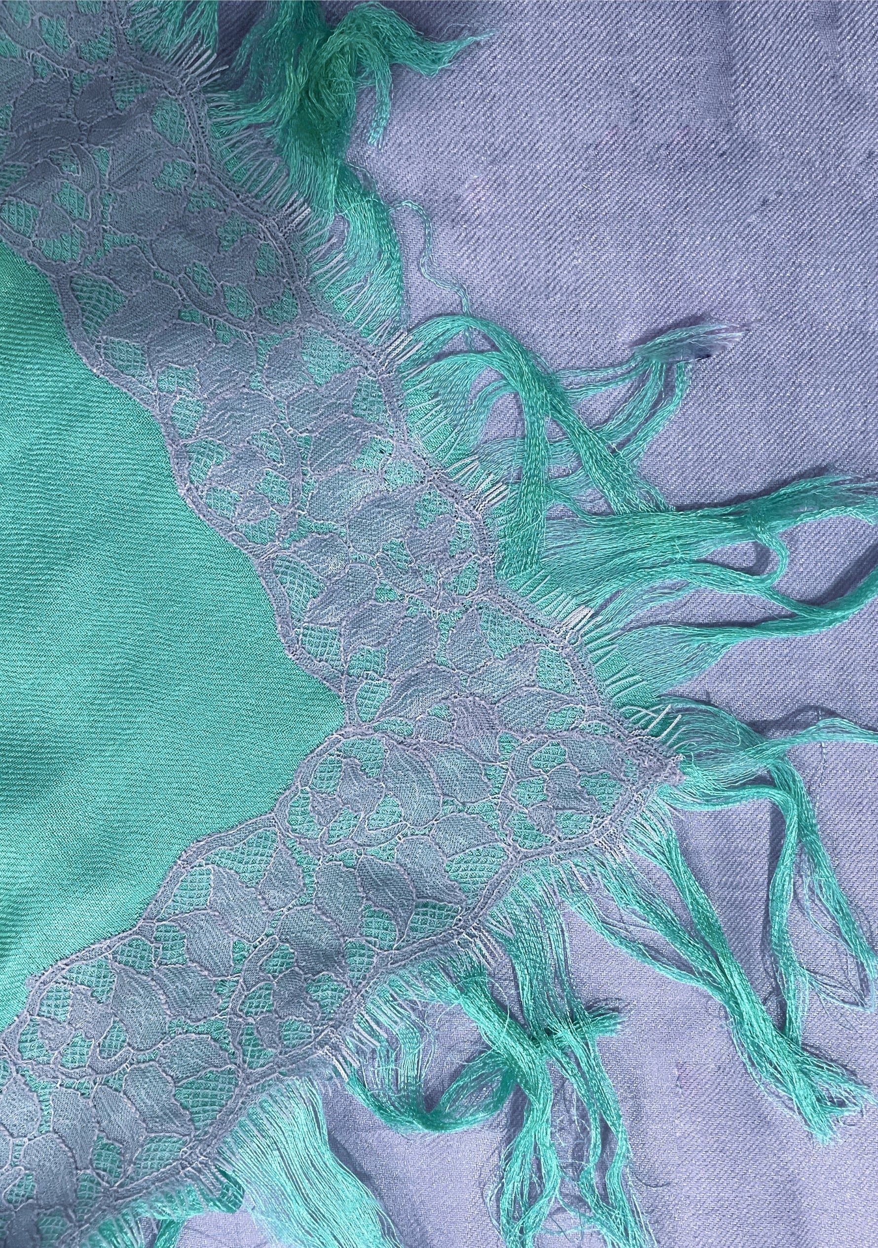 Close-up of the Maneesha Ruia Aqua Ombré Modal & Cashmere Scarf featuring lavender floral lace trim, aqua-to-lavender ombré fabric, and hand-knotted fringes.