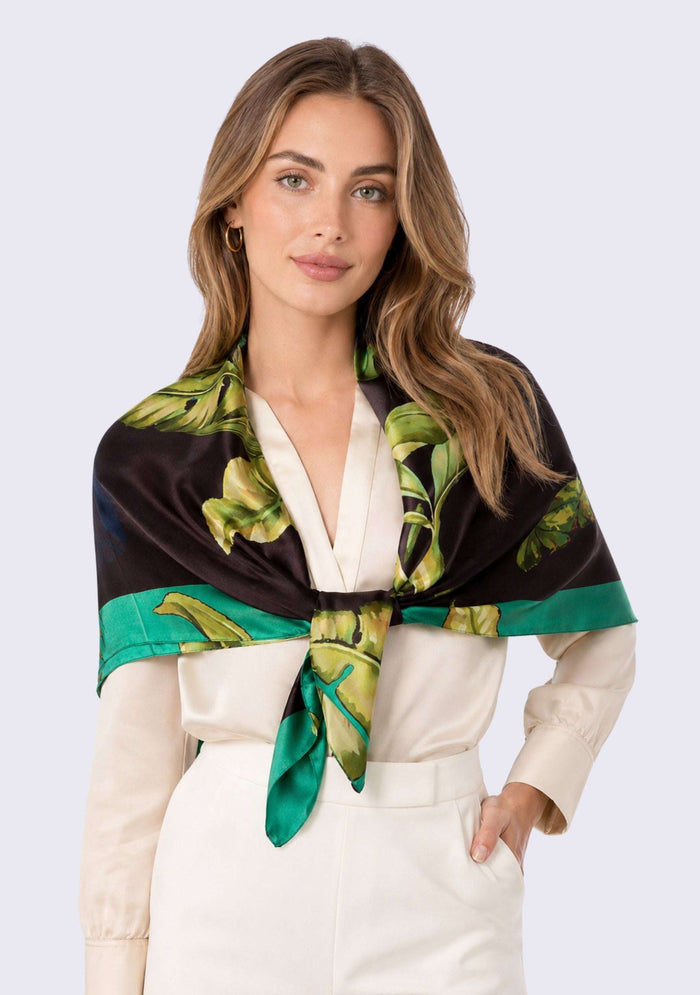 Cockatoo Print Silk Square Scarf by Maneesha Ruia tied over the shoulders, featuring tropical foliage and teal green accents on luxurious 100% silk.