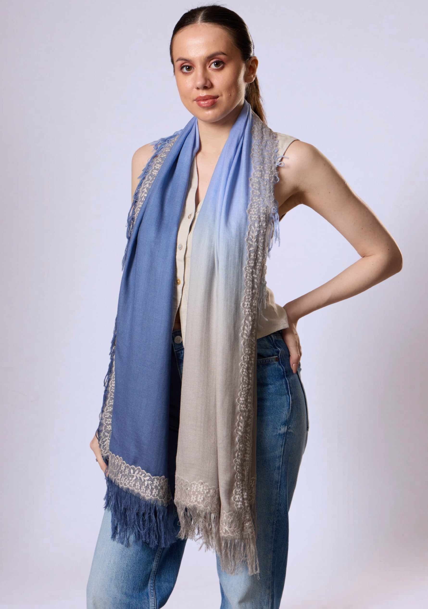 Maneesha Ruia Denim Ombré Modal & Cashmere Scarf with Mousse Lace Fringes, elegantly draped on a model, featuring a beige-to-denim blue ombré gradient with delicate lace trim and fringed edges.