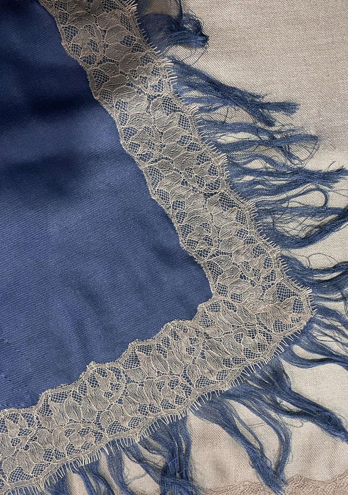 Close-up of the Maneesha Ruia Denim Ombré Modal & Cashmere Scarf featuring beige floral lace trim, a beige-to-denim blue ombré gradient, and soft hand-knotted fringes.