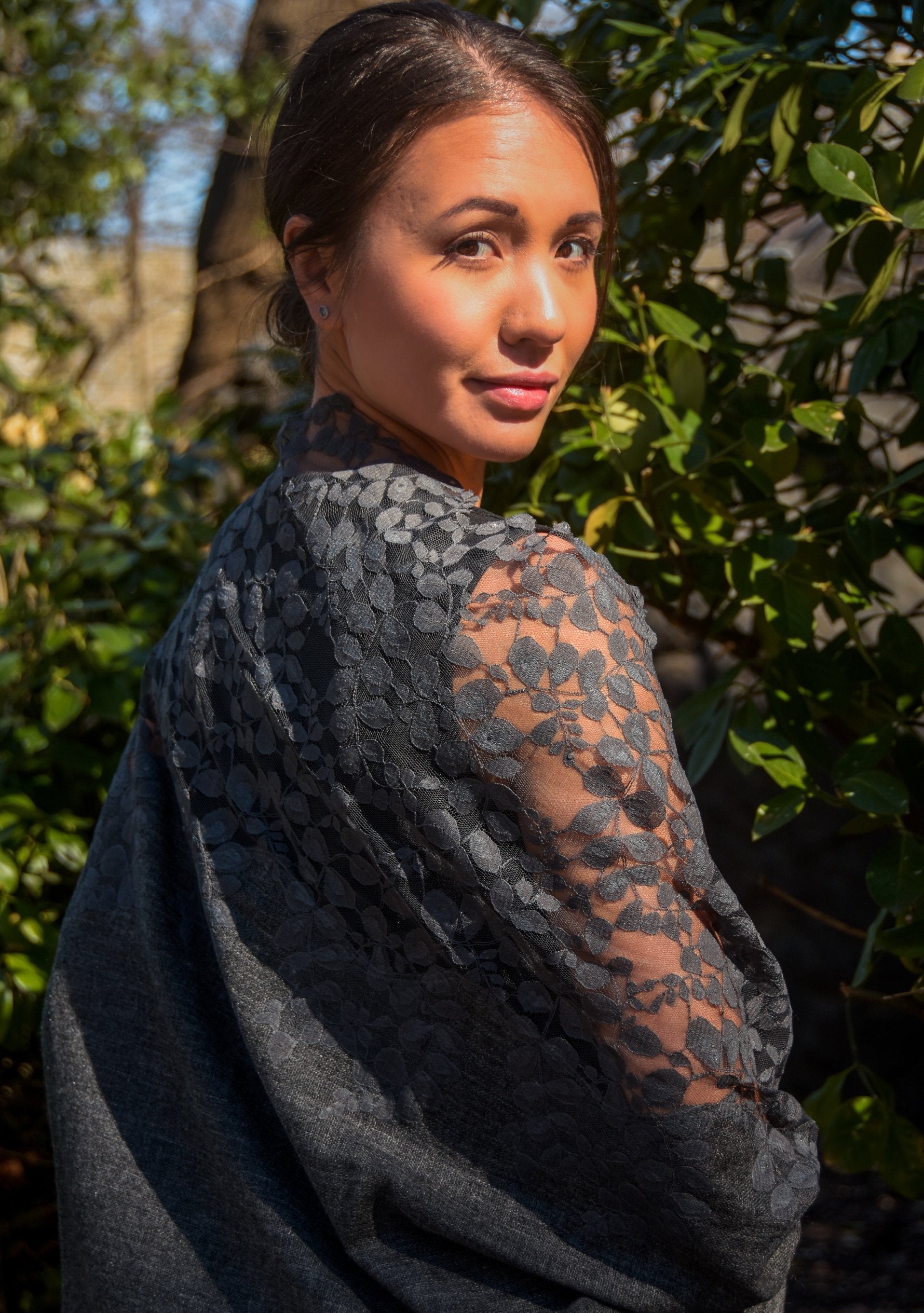 A woman wearing a dark grey fine wool scarf with a dark grey lace, with a blurred natural background
