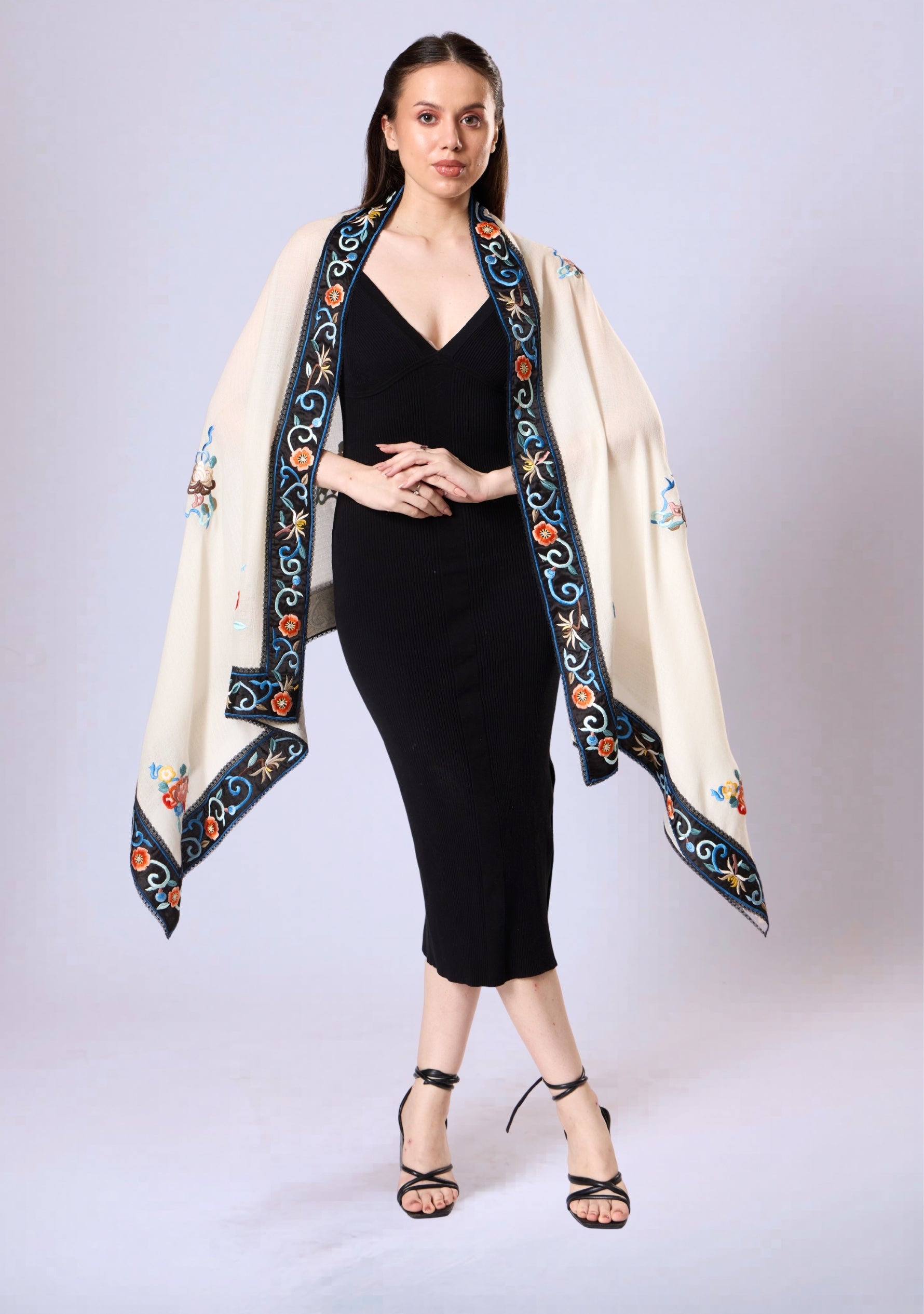 Woman wearing a black dress with an embroidered cream shawl on a white background