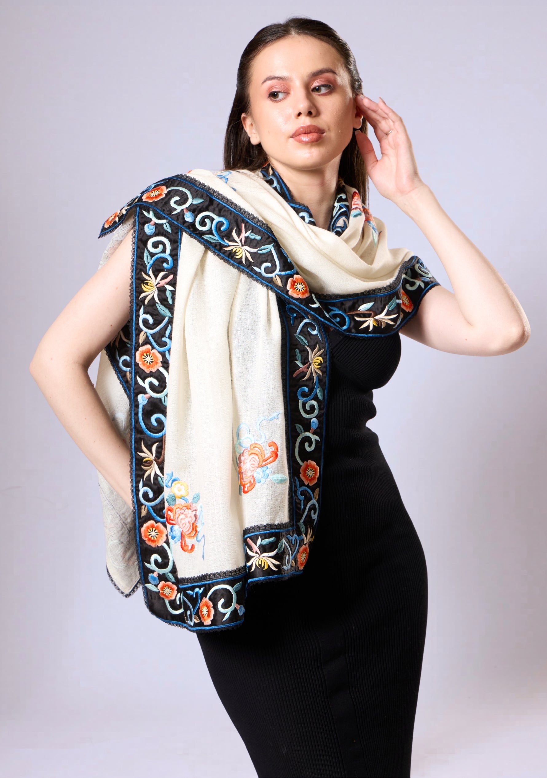 Woman wearing a black dress with a white embroidered scarf against a plain background