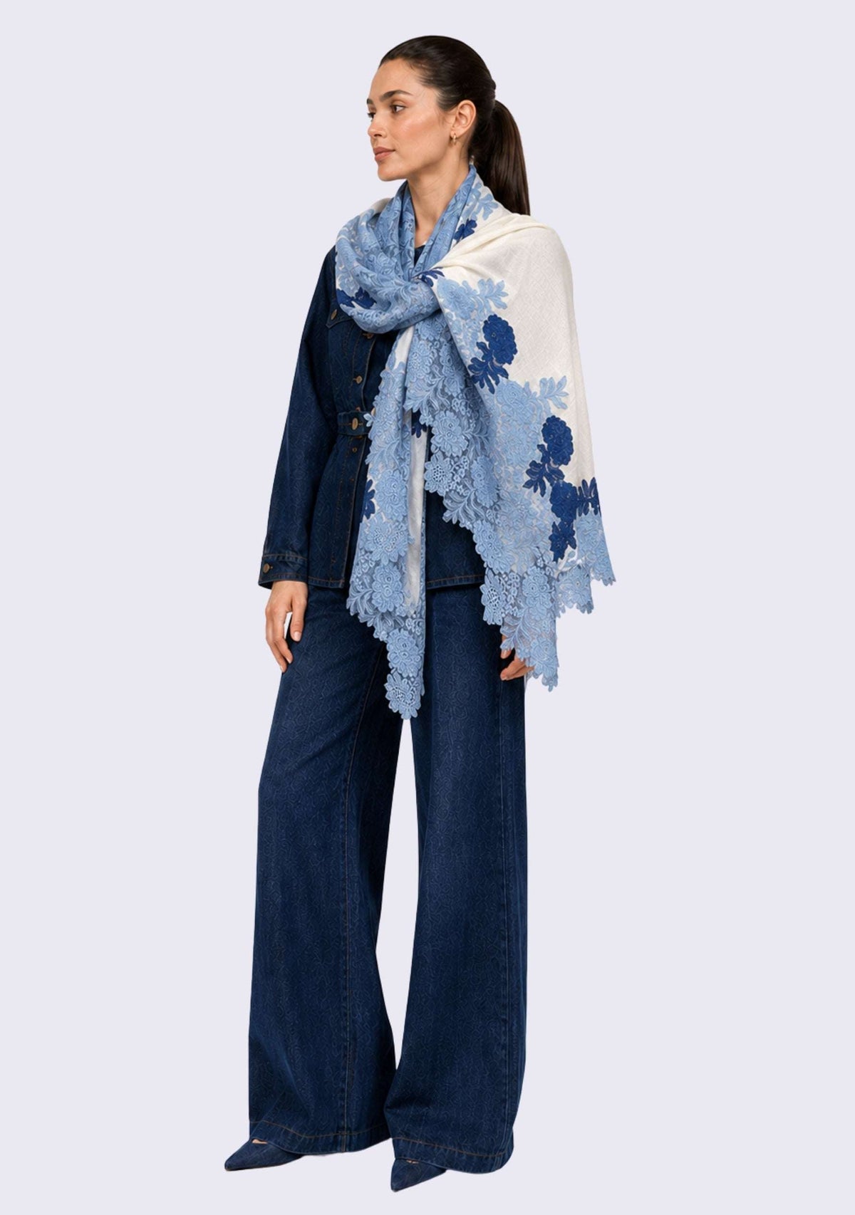 Female model wearing a luxury ivory wool and silk scarf with handcrafted steel blue and dark denim blue Chantilly floral lace, elegantly draped over a denim outfit to showcase its lightweight fabric, graceful drape, and intricate floral lace detailing.