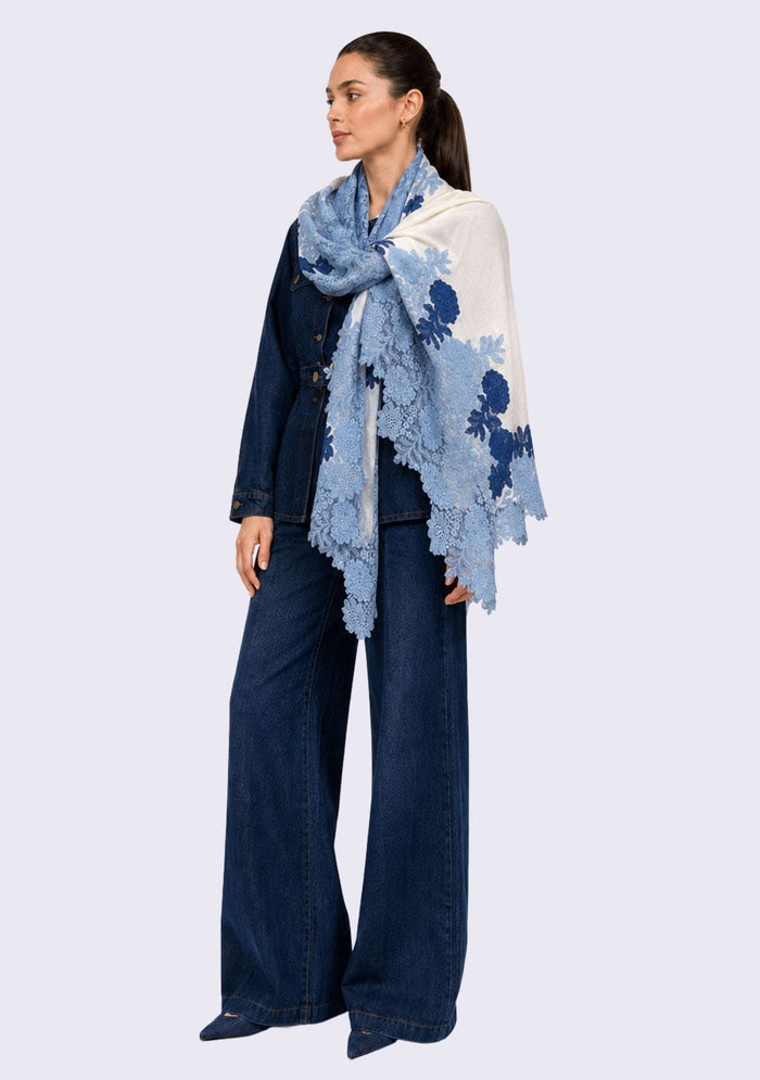 Female model wearing a luxury ivory wool and silk scarf with handcrafted steel blue and dark denim blue Chantilly floral lace, elegantly draped over a denim outfit to showcase its lightweight fabric, graceful drape, and intricate floral lace detailing.