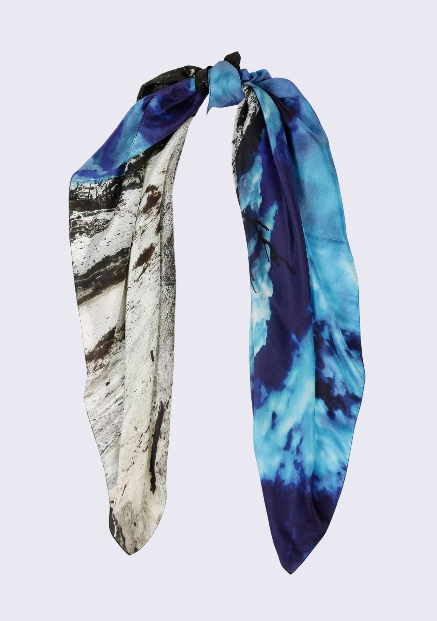 Mammoth Hot Springs Print Silk Square Scarf by Maneesha Ruia styled in a graceful knot, showcasing a scenic landscape print with vivid turquoise-blue skies, black accents, and white geothermal terrain on luxurious 100% silk.