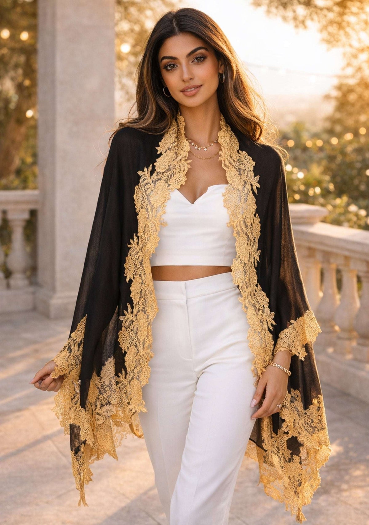 Woman wearing a black and gold lace kimono over a white outfit in an outdoor setting.