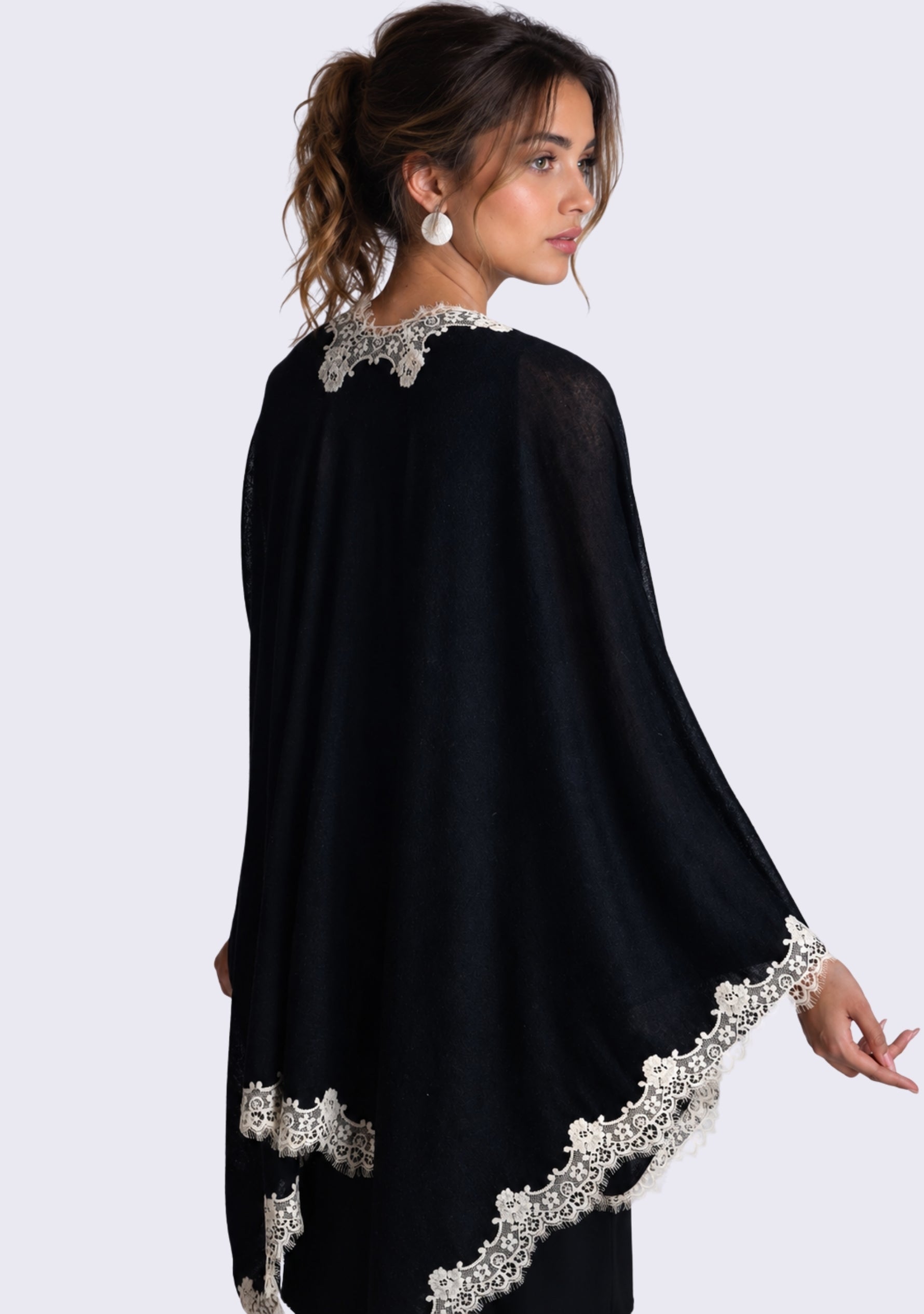 A woman wearing a Black merino wool cape with beige lace photographed against a light gray studio background.