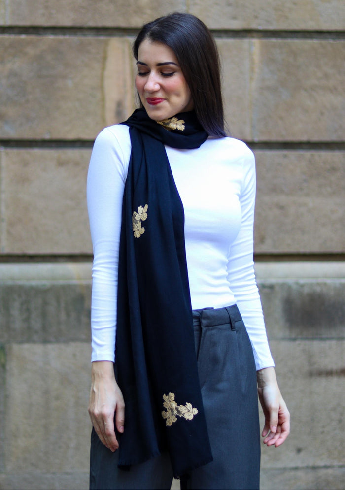 Woman wearing a black scarf with gold brooches against a stone wall.