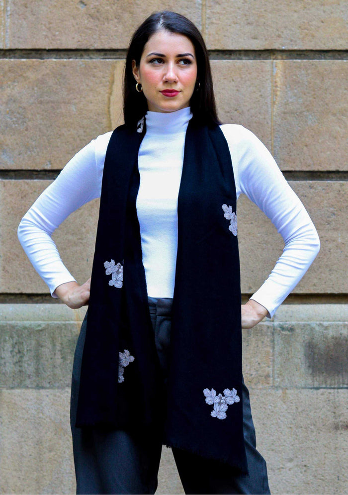 Woman wearing a black vest with white floral patterns against a stone wall.
