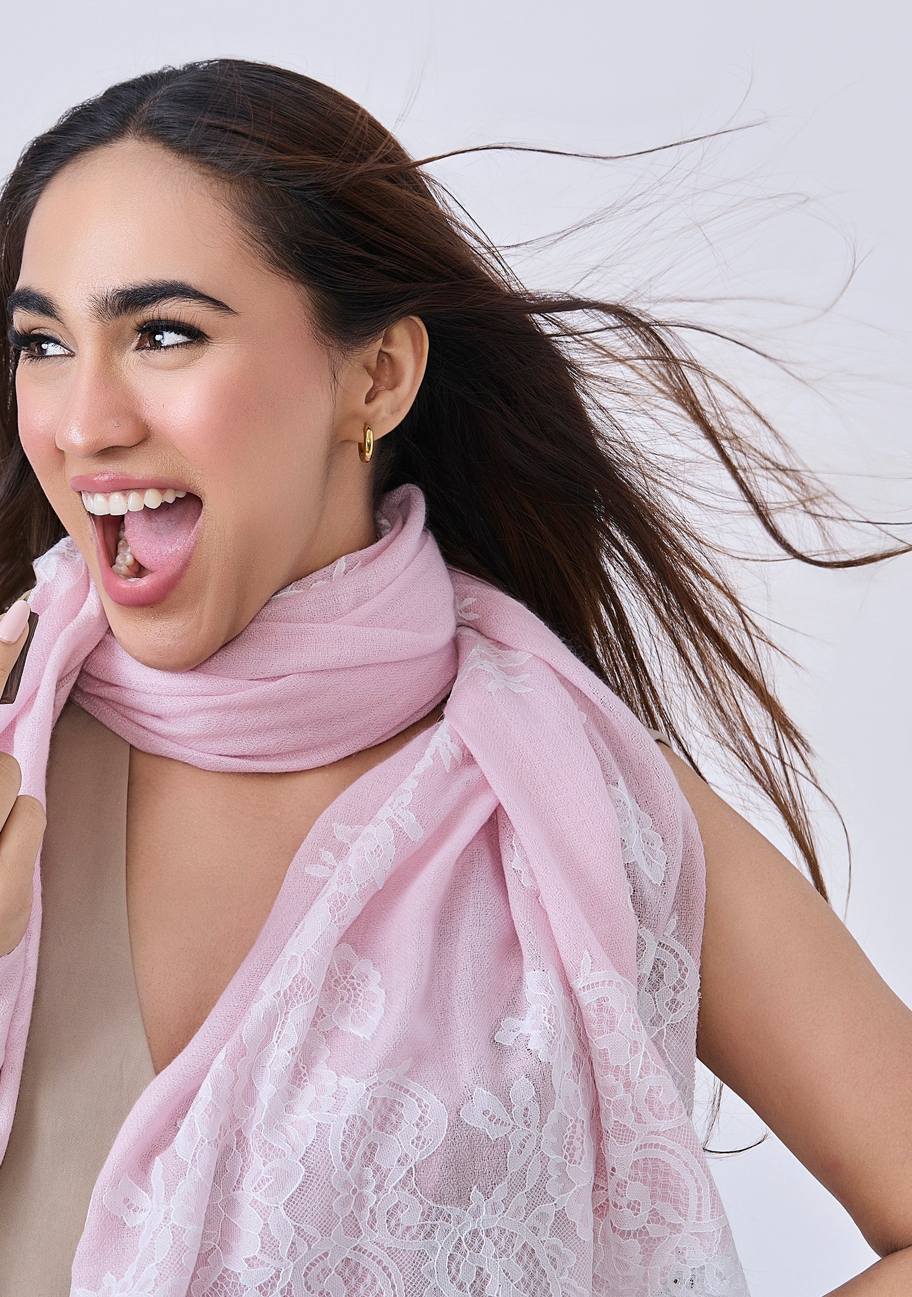 A woman wearing a Maneesha Ruia Baby Pink Cashmere Scarf — delicate white filigree lace on luxuriously soft cashmere details around her neck.