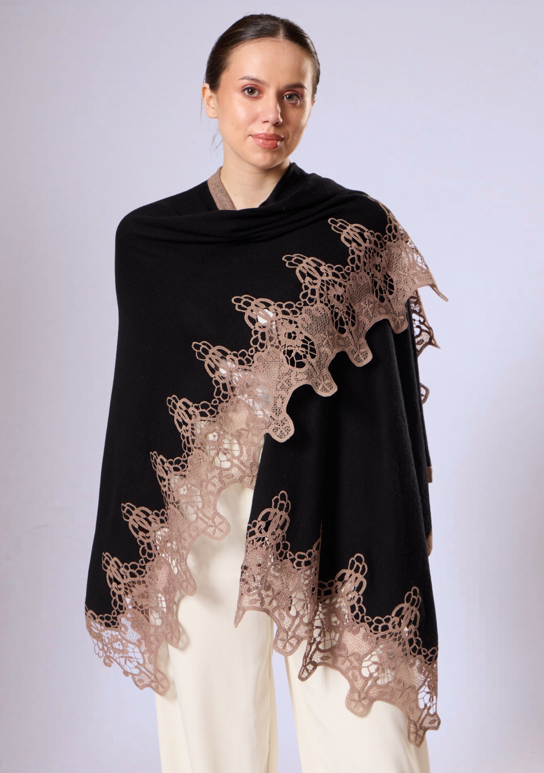 Woman wearing a black wool cape with floral lace details on a white background