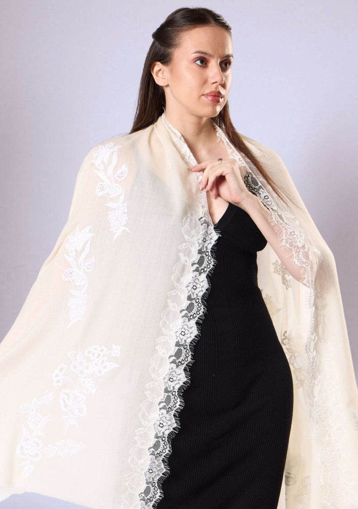 Woman wearing a white shawl with lace trim over a black dress on a plain background